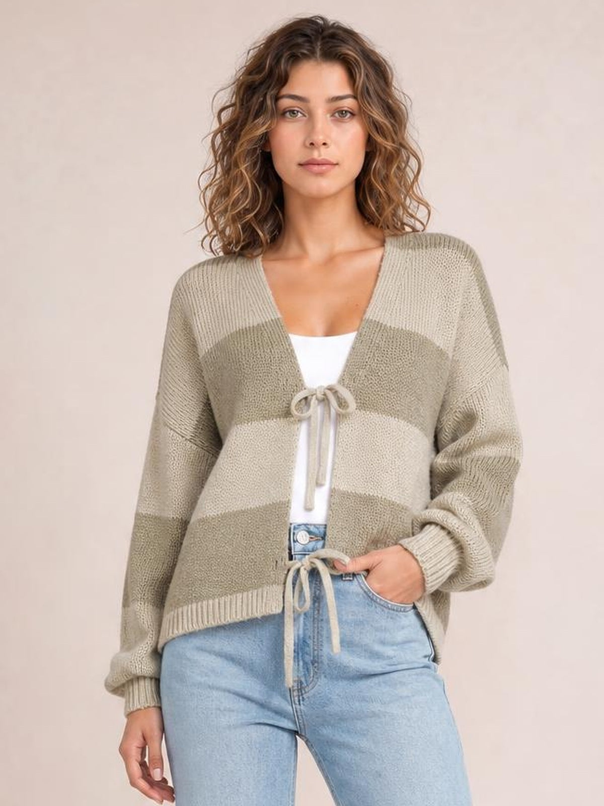 Model poses in a beige and taupe striped color-block sweater cardigan with a tie front, V-neckline, long sleeves, and relaxed silhouette.