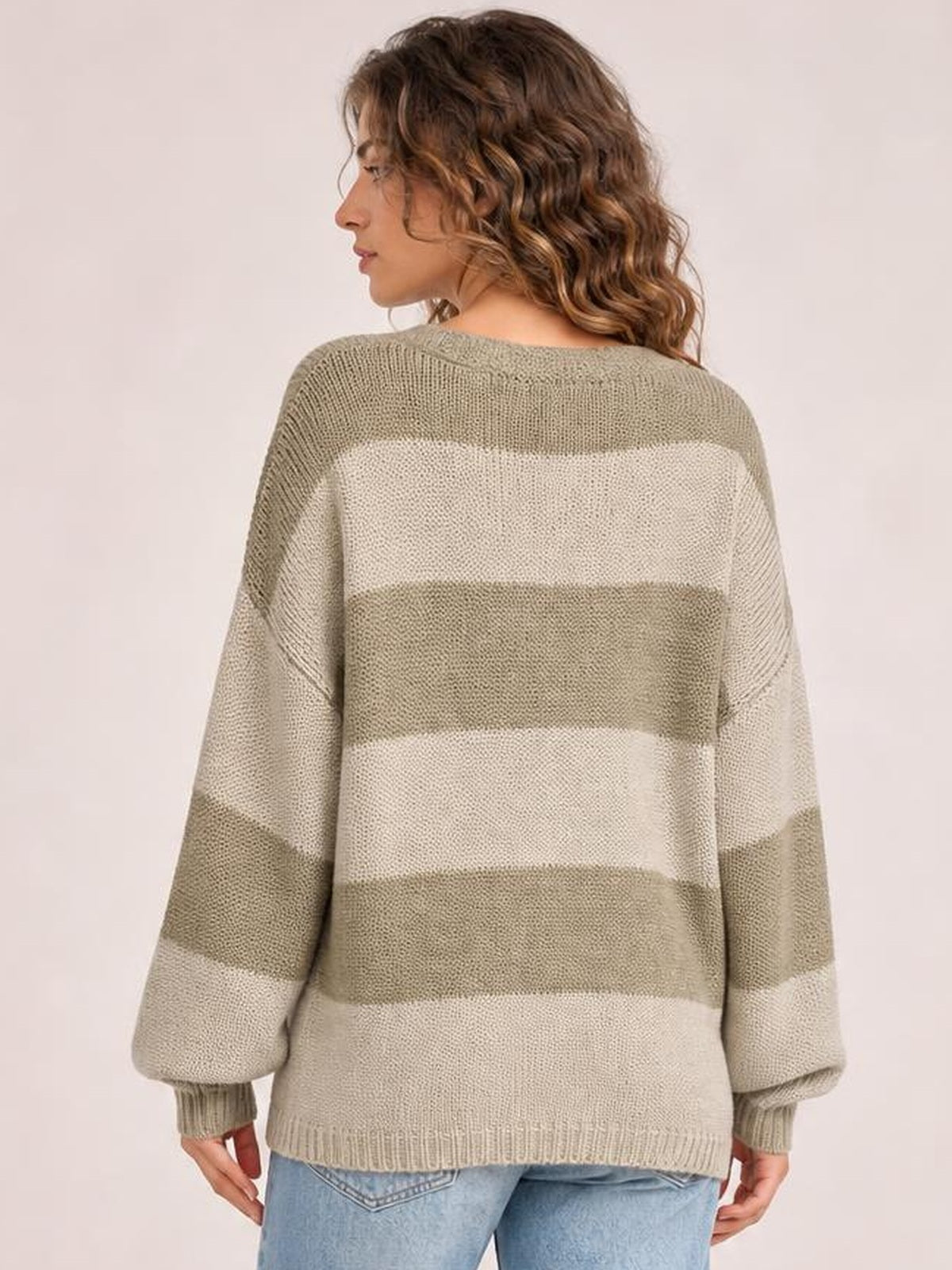 Model shown from the back in a relaxed, oversized striped color block sweater cardigan with wide beige and cream bands, long sleeves, and ribbed cuffs and hem.
