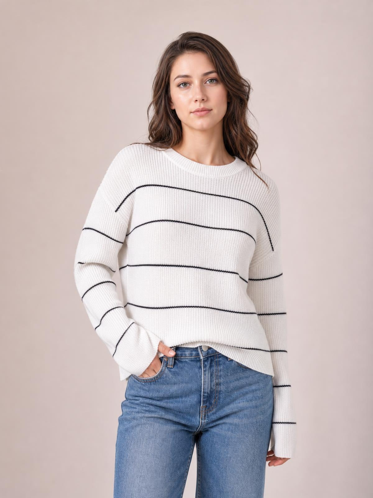 Model poses with one hand in her jeans pocket, wearing a white striped crew neck sweater with dropped shoulders, relaxed fit, and ribbed knit construction.
