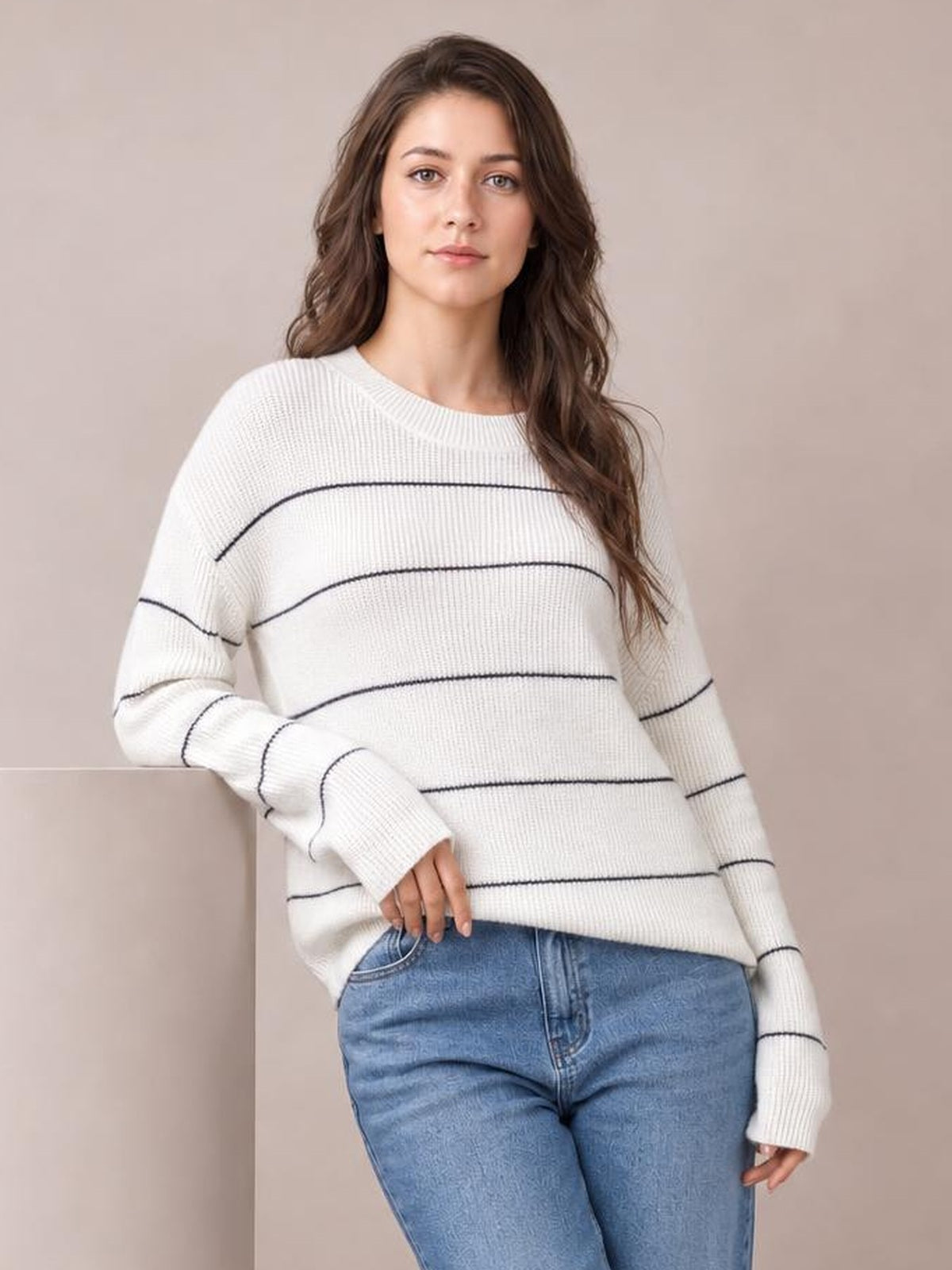 A model leans casually in a white ribbed knit striped crew neck sweater with dropped shoulders, long sleeves, and a relaxed silhouette.