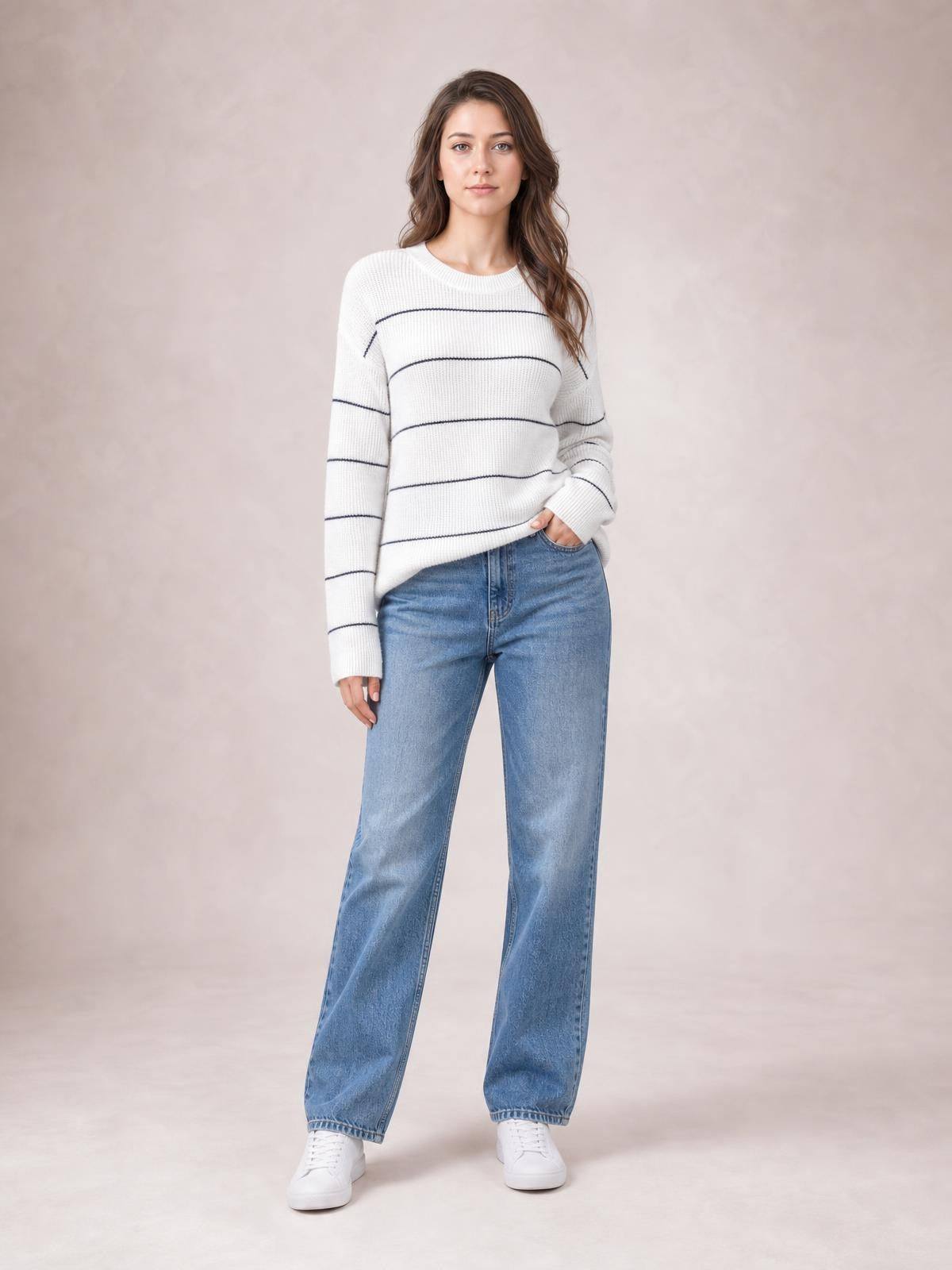Model wearing a white striped crew neck sweater with dropped shoulders, ribbed cuffs and hem, a relaxed silhouette, and one hand in her jeans pocket.