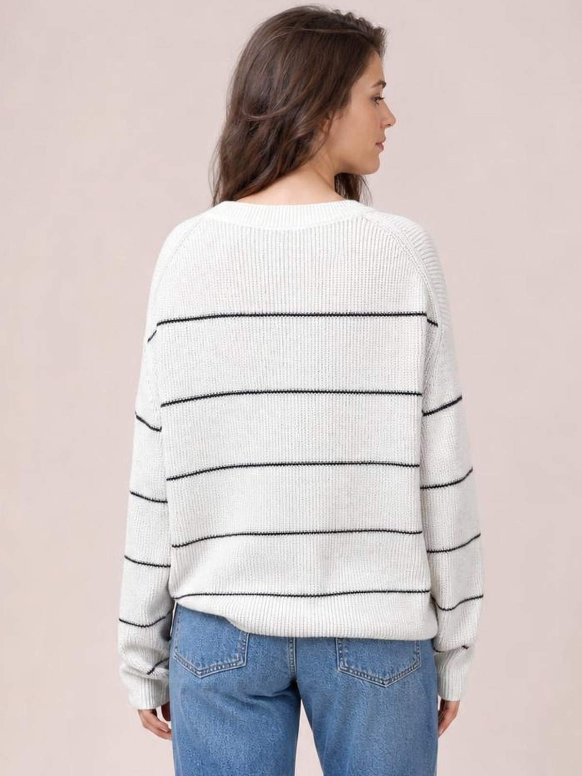 Model shown from behind wears a white striped crew neck sweater with dropped shoulders, relaxed fit, ribbed trim, and long sleeves.