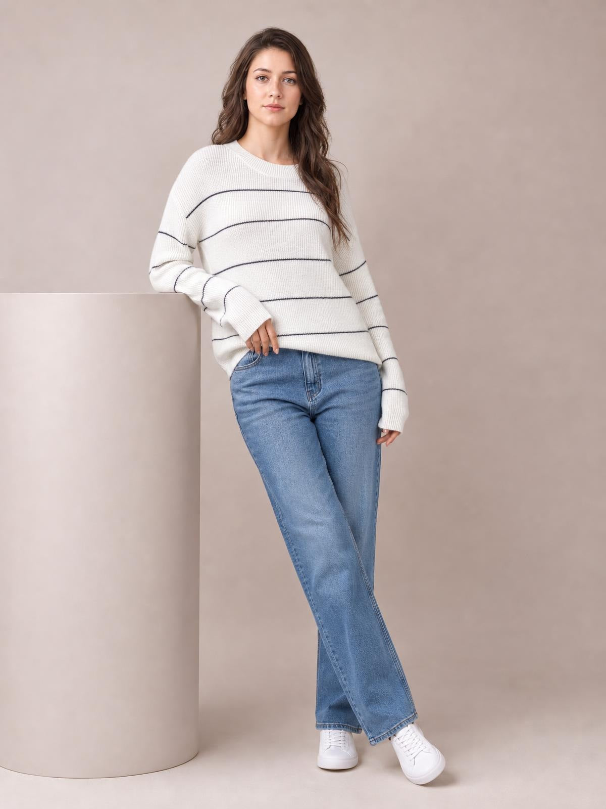 Model wears a white striped crew neck sweater with dropped shoulders, relaxed silhouette, ribbed trim, long sleeves, and blue jeans.