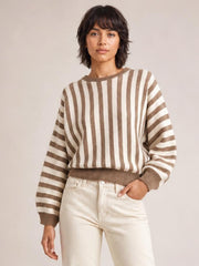 Model wearing a brown and cream striped crew neck sweater with a relaxed silhouette, ribbed collar, cuffs, and hem, posing with one hand in her pocket.