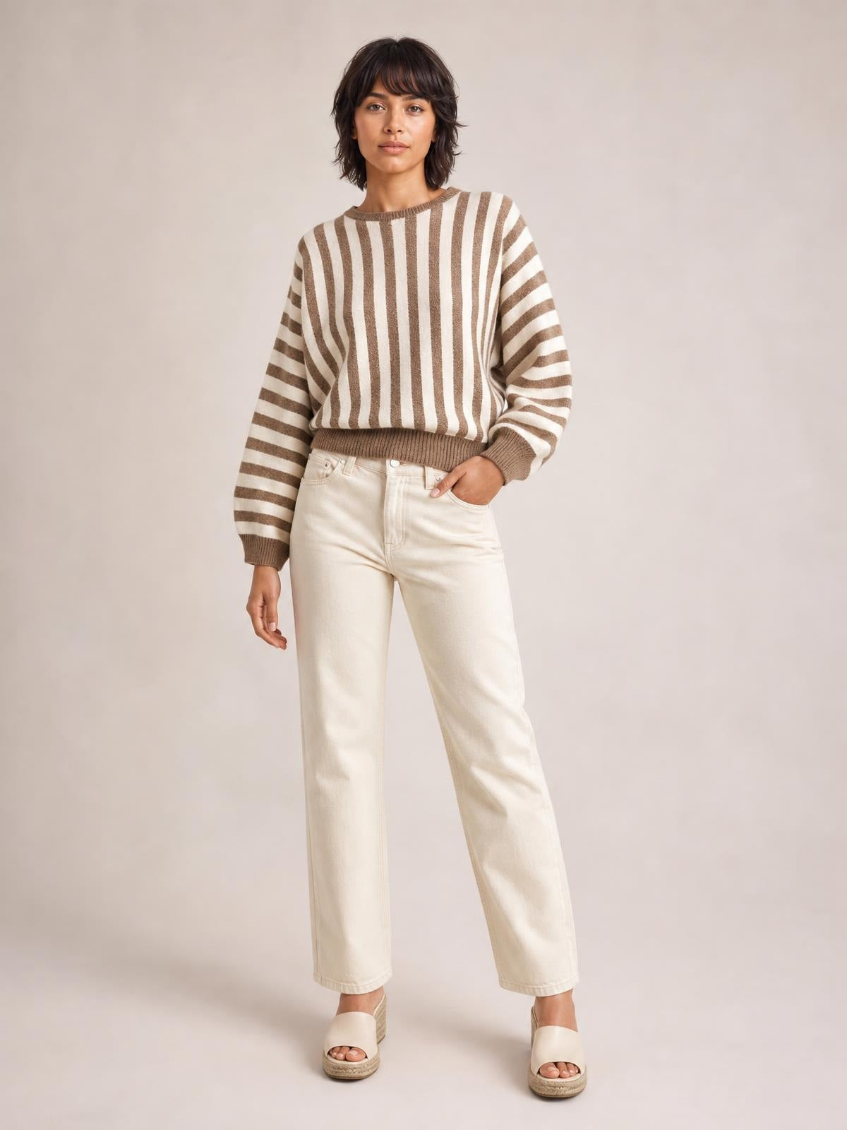 Model wearing a ribbed striped crew neck sweater in taupe and cream with a relaxed silhouette, long sleeves, and ribbed cuffs and hem.