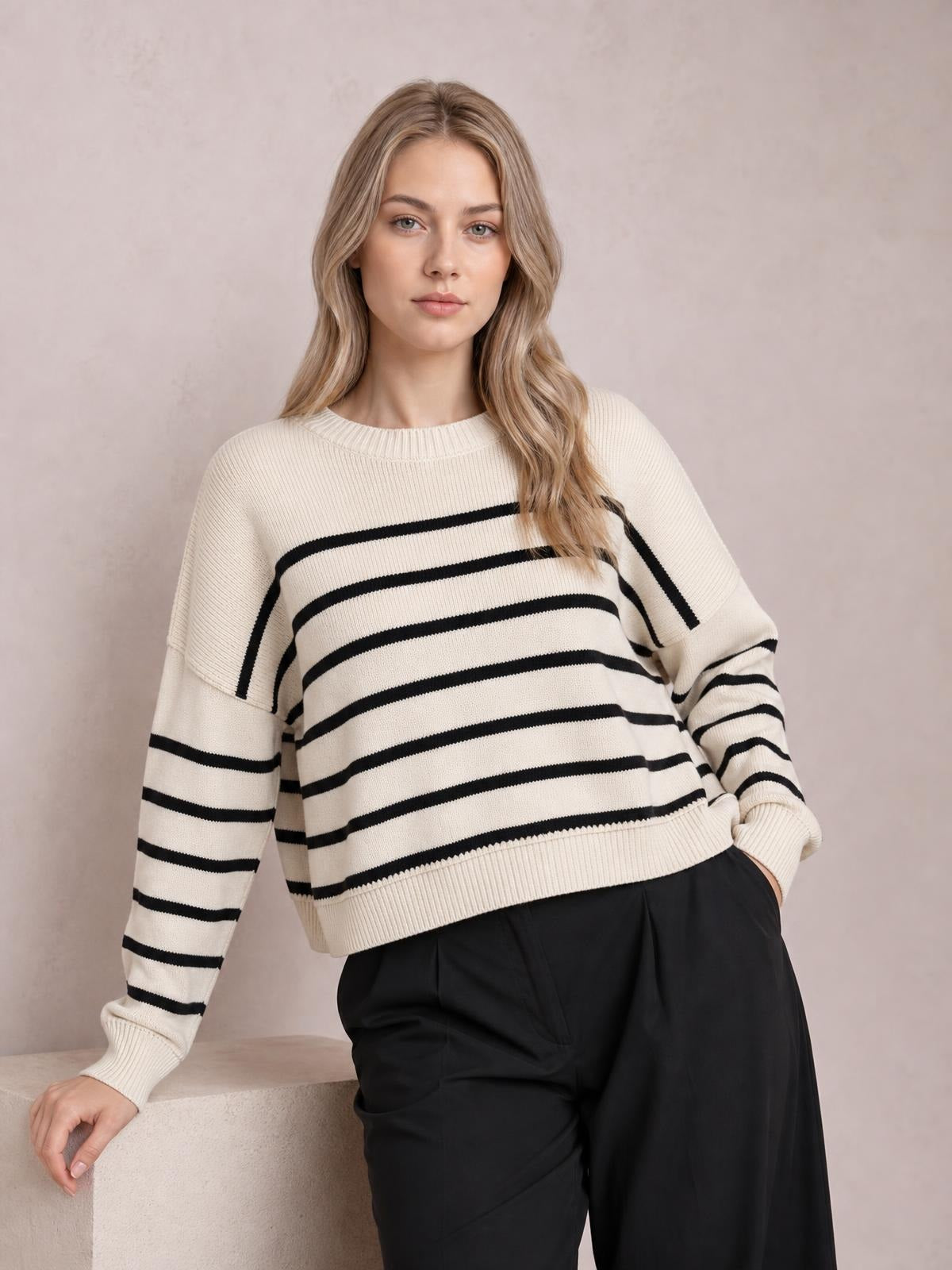 Model wearing a cream striped round-neck pullover sweater with black horizontal stripes, dropped shoulders, long lantern sleeves, ribbed cuffs and hem, and a relaxed silhouette.