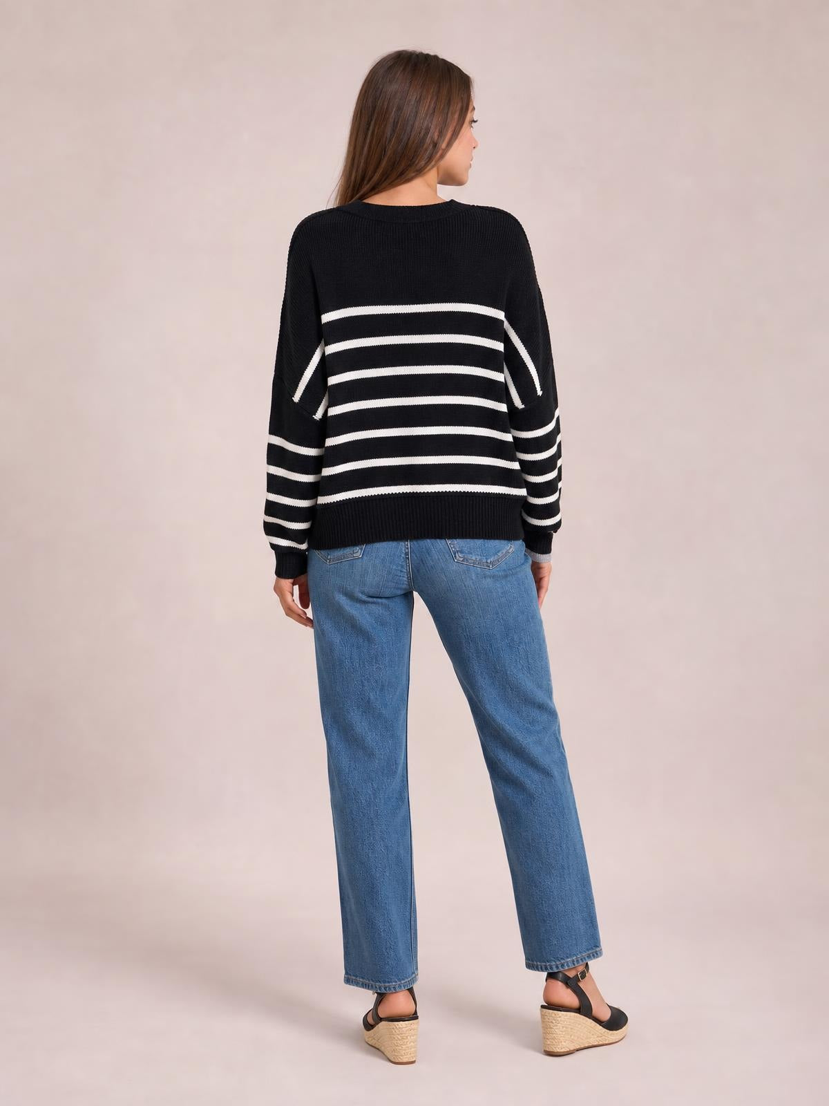 A model stands turned away in a black-and-white striped pullover sweater with a round neck, dropped shoulders, long lantern sleeves, and a relaxed regular silhouette.