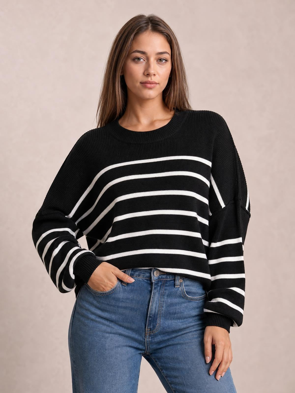 Model poses with one hand in her jeans pocket wearing a black-and-white striped round-neck pullover sweater with dropped shoulders and relaxed lantern sleeves.