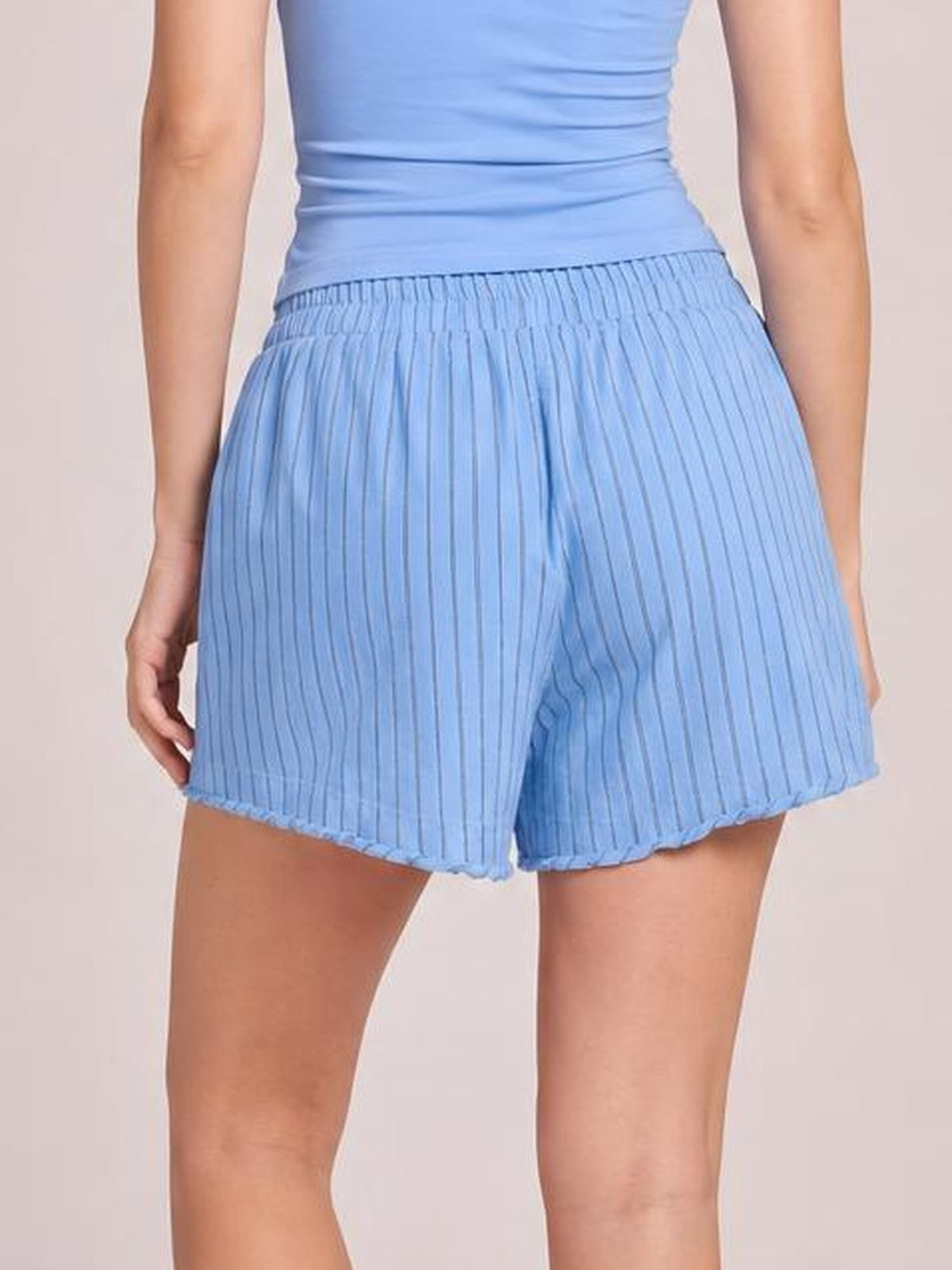 Model stands wearing light blue striped elastic waist shorts with a gathered waistband, relaxed loose silhouette, and mid-thigh hem.