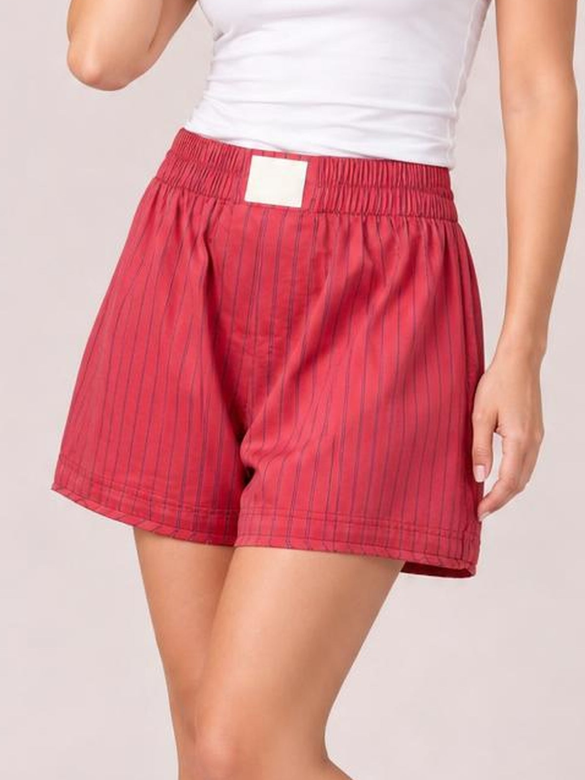 A cropped model wears red striped elastic-waist shorts with a relaxed, loose silhouette, gathered waistband, and straight hems.