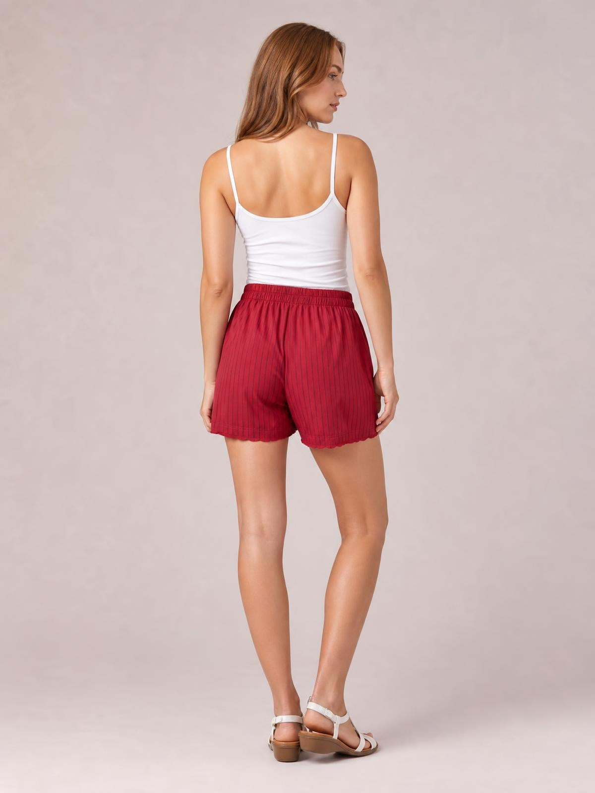 A model poses in a rear three-quarter view wearing red striped elastic-waist shorts with a relaxed mid-thigh silhouette and softly gathered waistband.