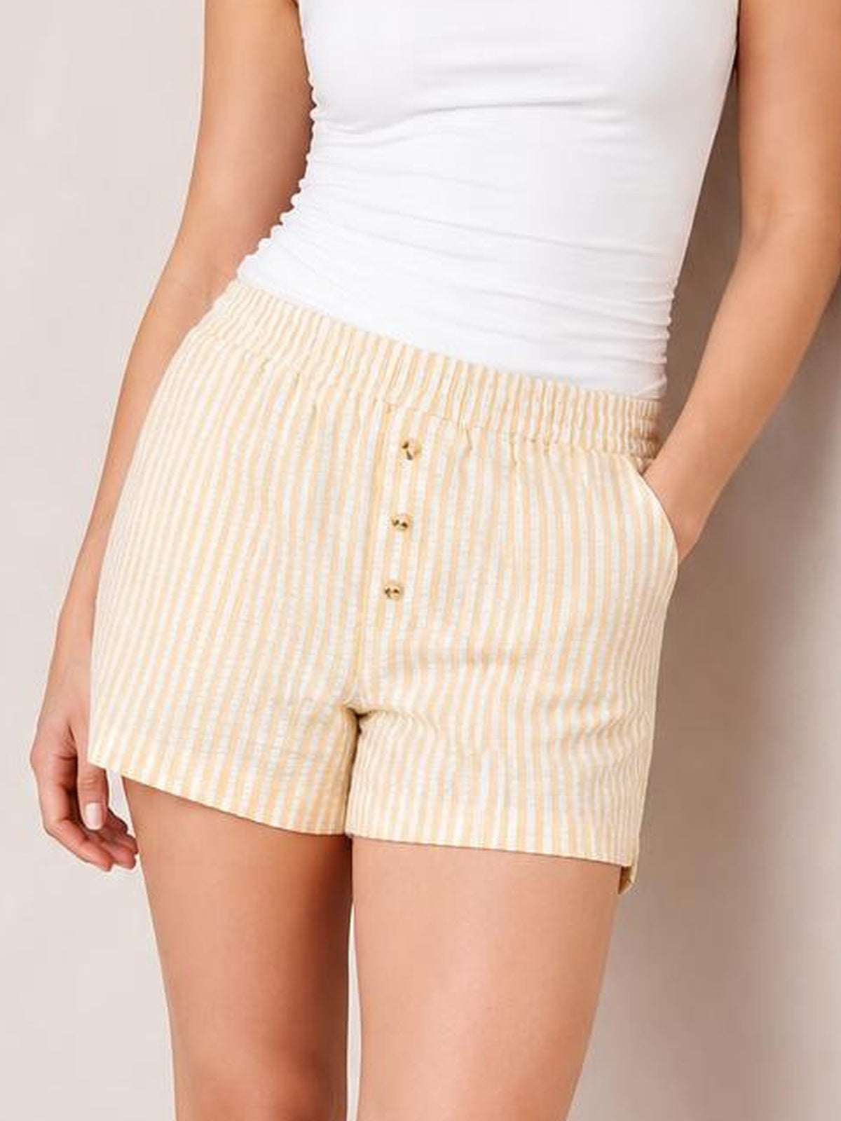 Model wearing cream striped elastic-waist shorts with a relaxed straight-leg silhouette, side pockets, and decorative front buttons.