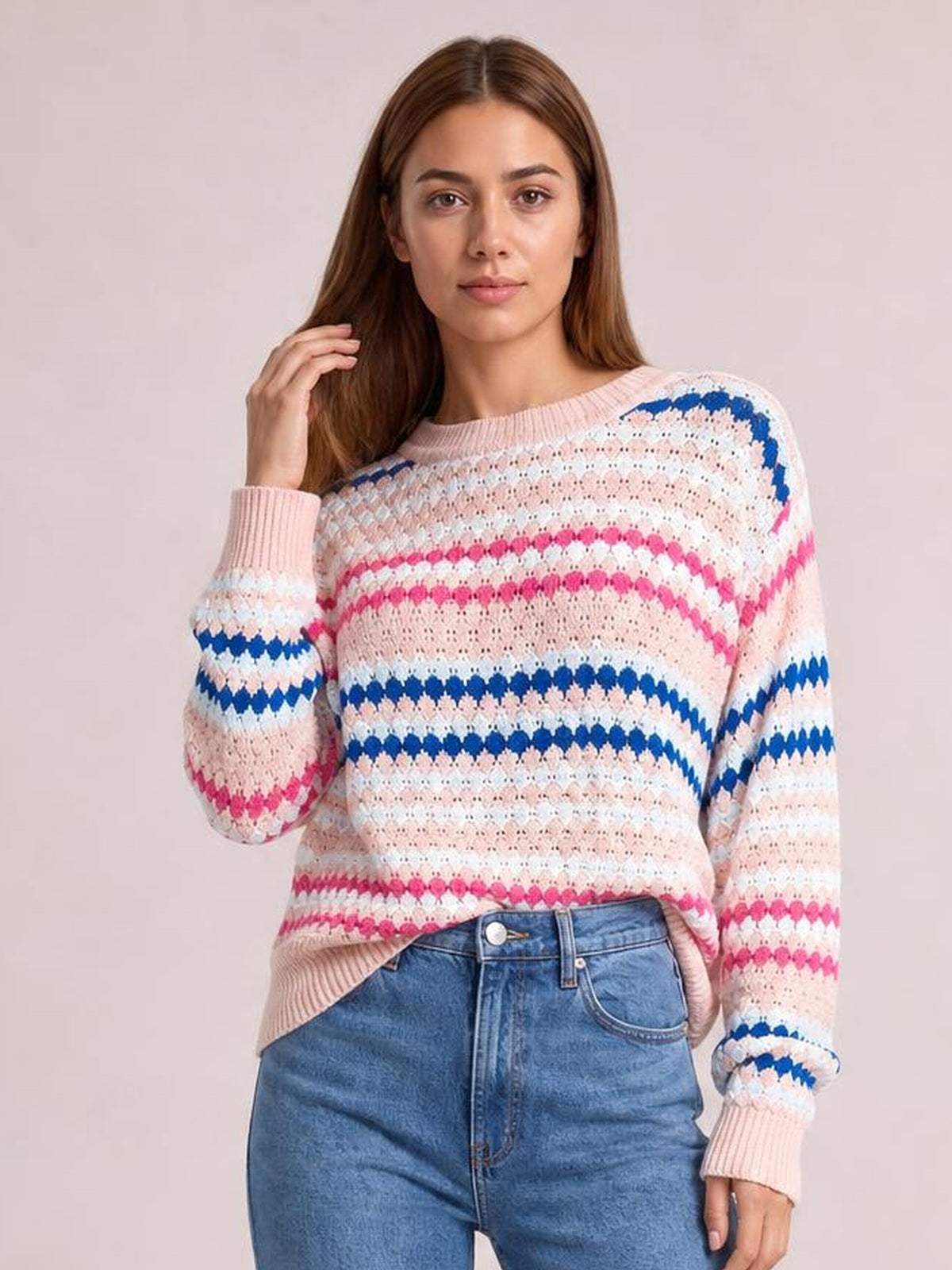 Model poses in a relaxed striped geometric pattern sweater with pink, white, and blue knit bands, a crew neck, long sleeves, and ribbed cuffs.