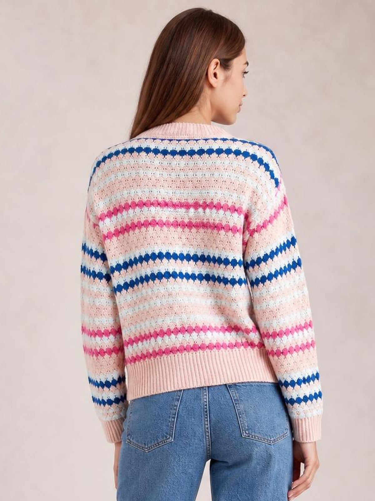 Model shown from behind in a relaxed striped geometric pattern sweater with cream, pink, and blue bands, ribbed collar, cuffs, and hem.