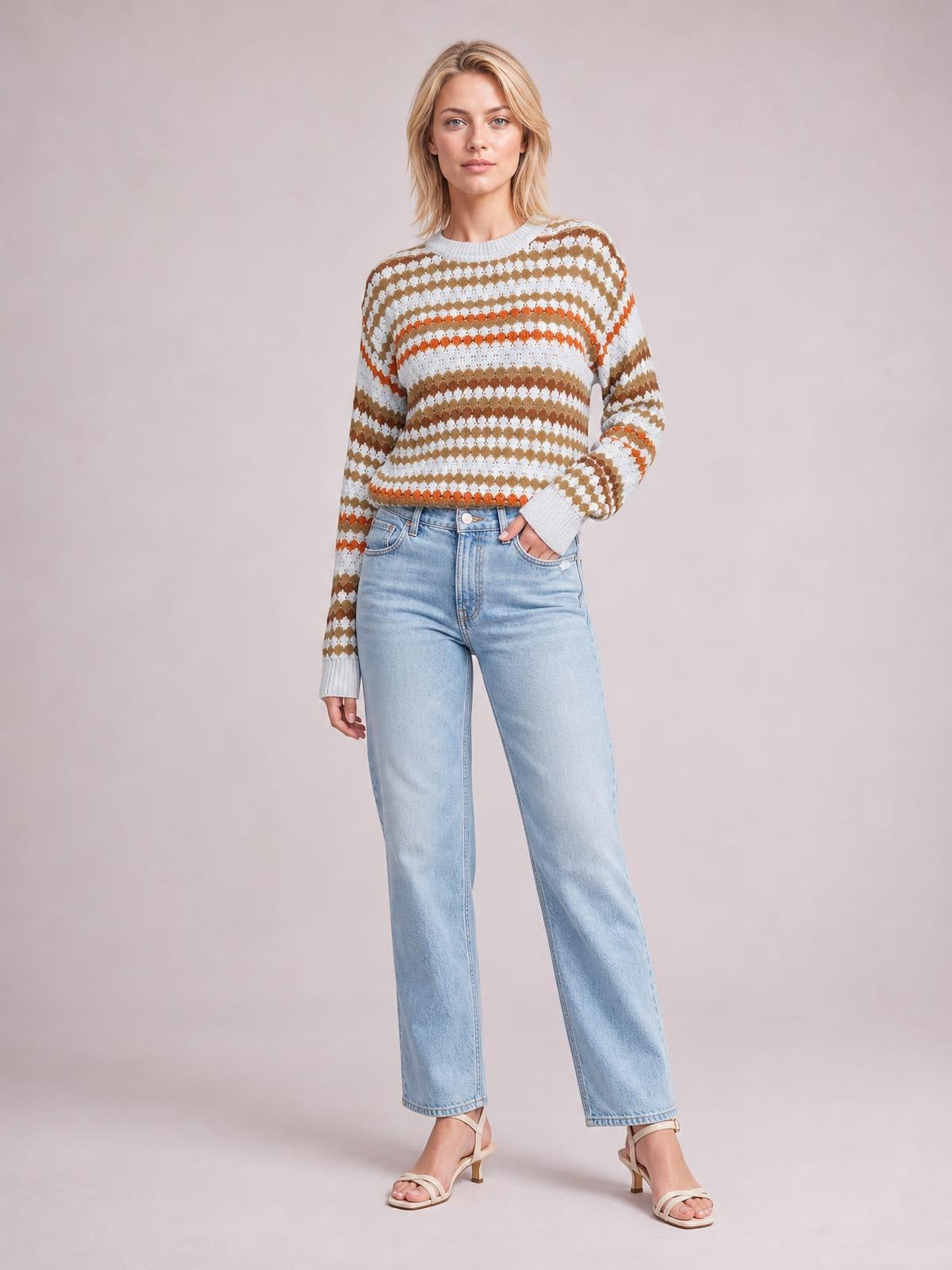 Model poses in a relaxed stance wearing a cream striped geometric pattern sweater with a crew neck, ribbed cuffs, and a relaxed silhouette.