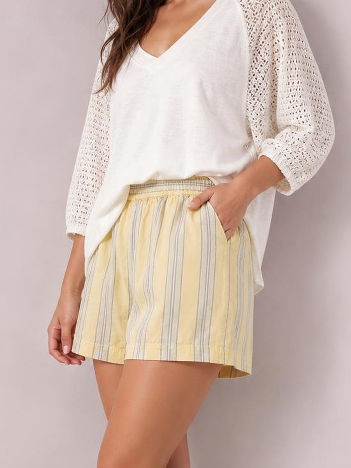 A model poses in yellow high-waist summer shorts with vertical gray stripes, a relaxed silhouette, gathered waistband, and convenient side pockets.