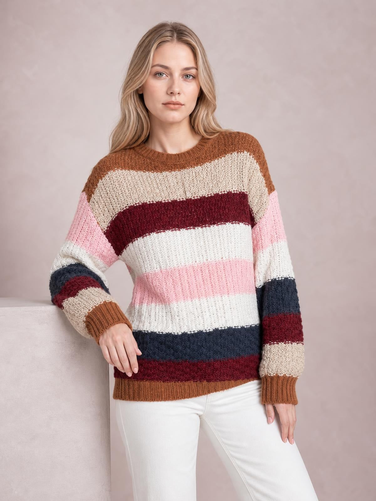 A model wears a multicolored striped knit sweater with a round neck, dropped shoulders, ribbed cuffs and hem, and a relaxed silhouette while leaning casually.