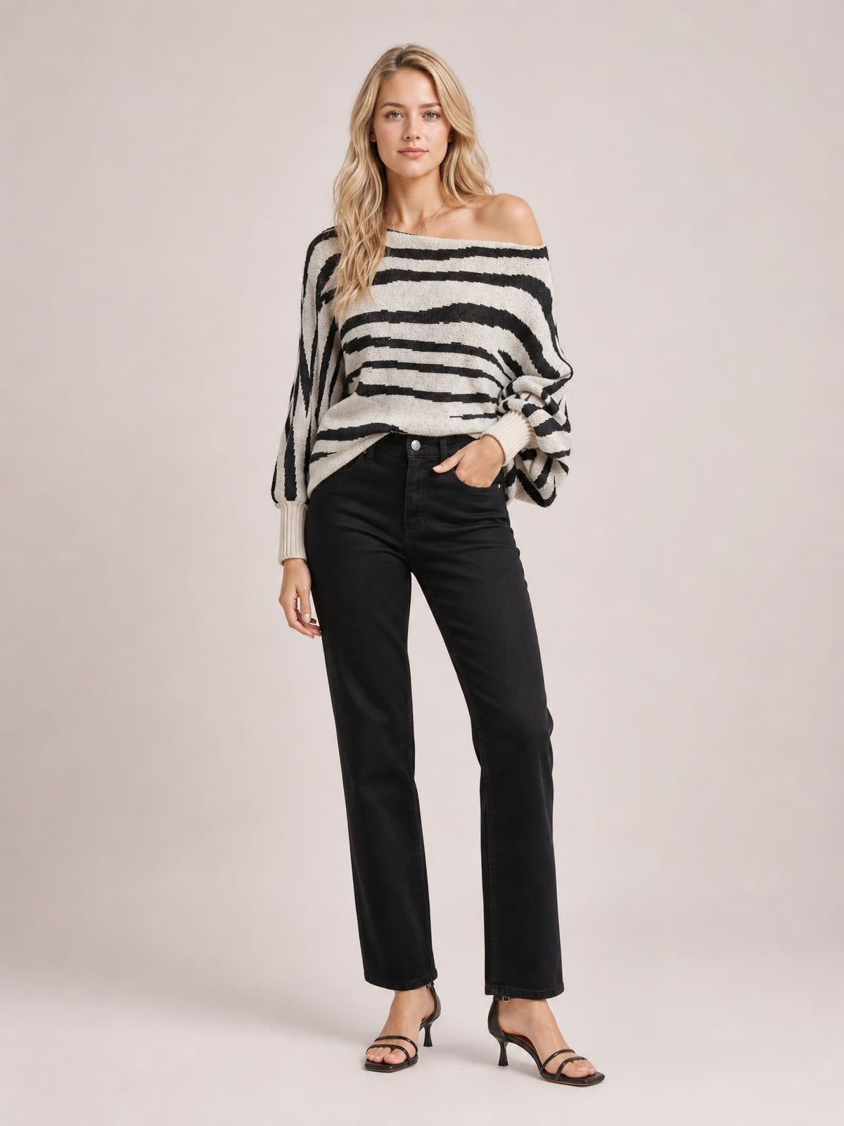 A model wears a black-and-white striped lantern sleeve sweater with a relaxed off-shoulder neckline, voluminous sleeves, ribbed cuffs, and one hand in her pocket.
