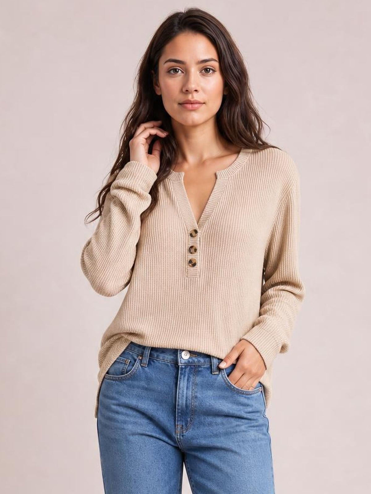 A model wears a beige long-sleeve T-shirt with ribbed texture, a notched neckline, three-button placket, relaxed silhouette, and one hand in her pocket.