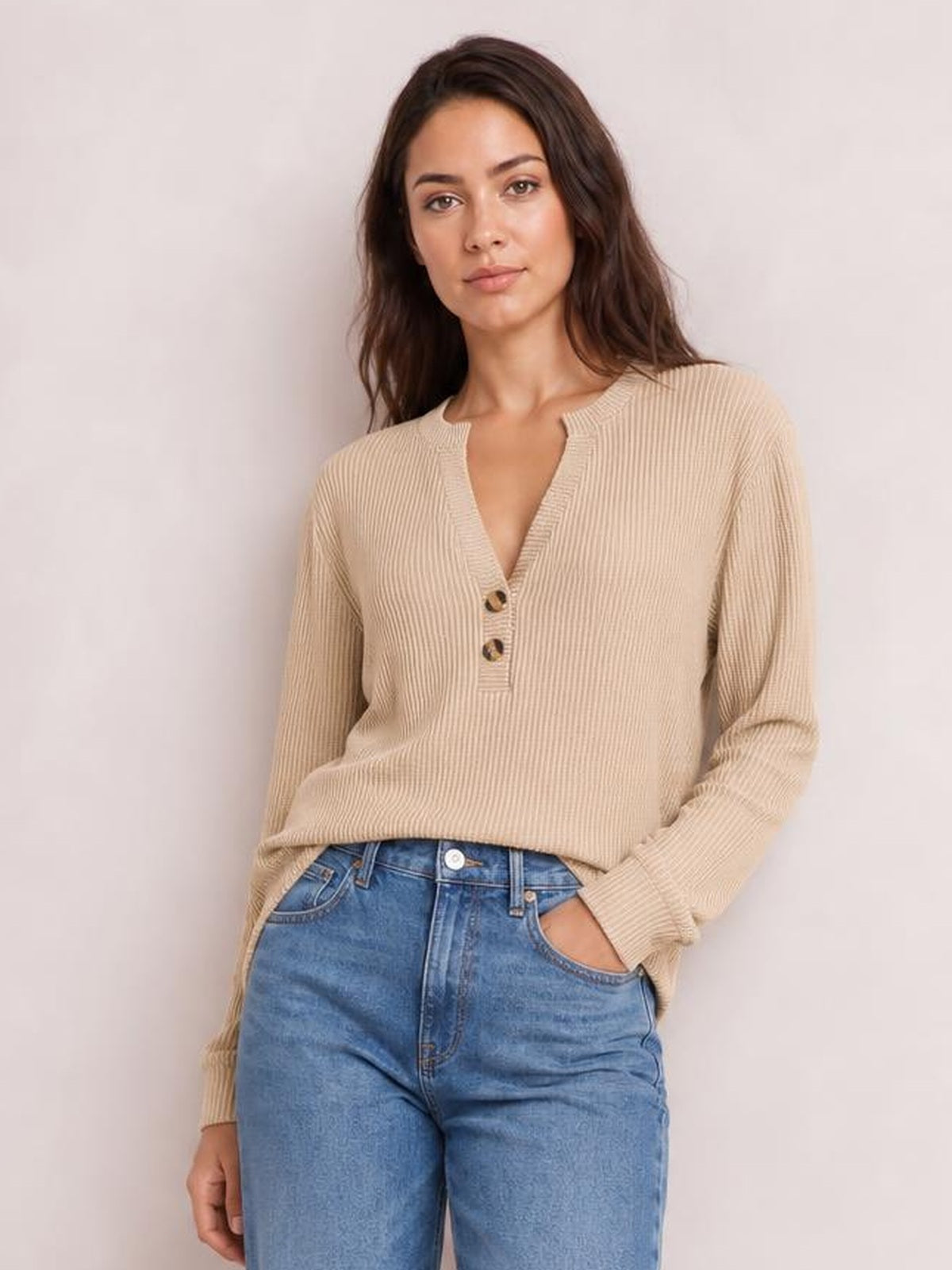 Model wearing a beige striped notched long sleeve T-shirt with fine ribbed texture, button accents, and a relaxed silhouette, posing with one hand in her jeans pocket.