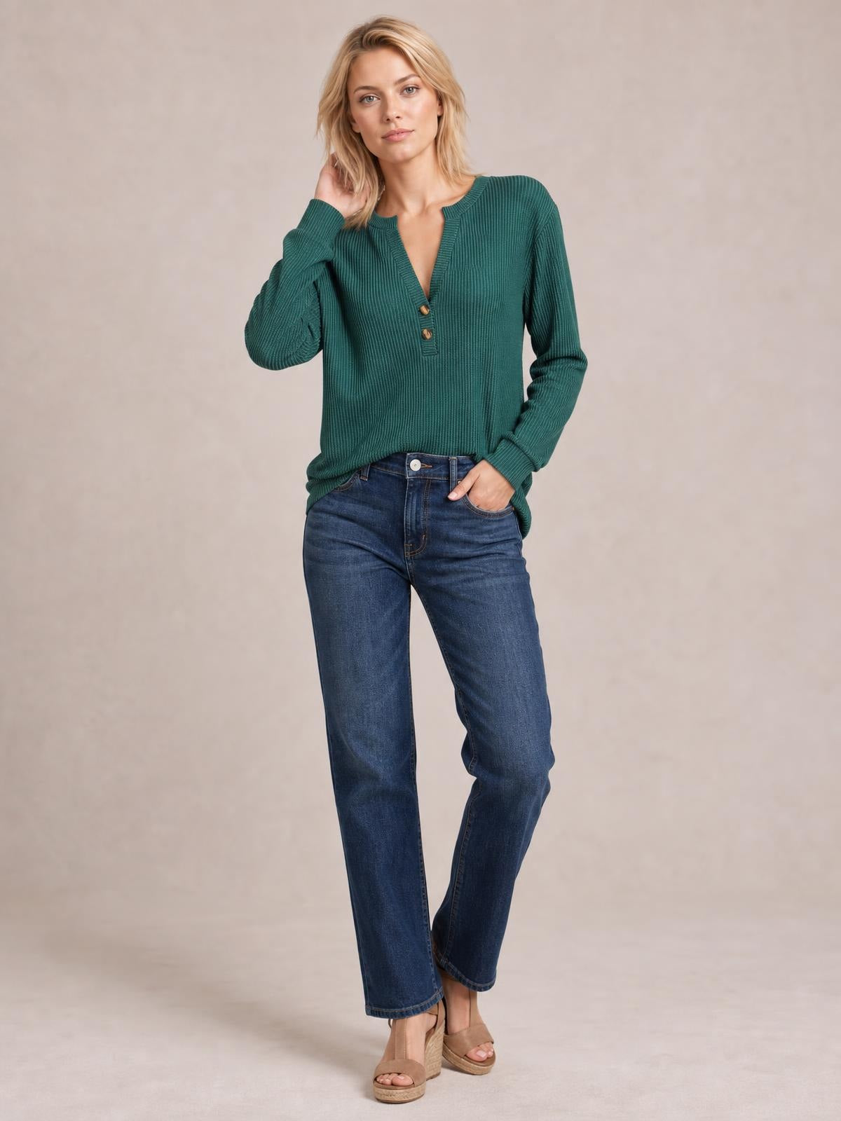 Model wears a green striped notched long sleeve T-shirt with a relaxed silhouette, ribbed texture, and button accents, posing with one hand in her pocket.