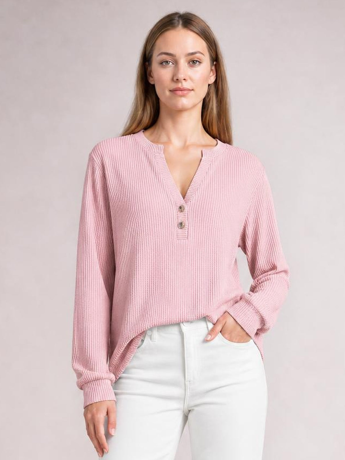 A model poses in a pink striped notched long sleeve T-shirt with a relaxed silhouette, ribbed cuffs, and a button-accented neckline.