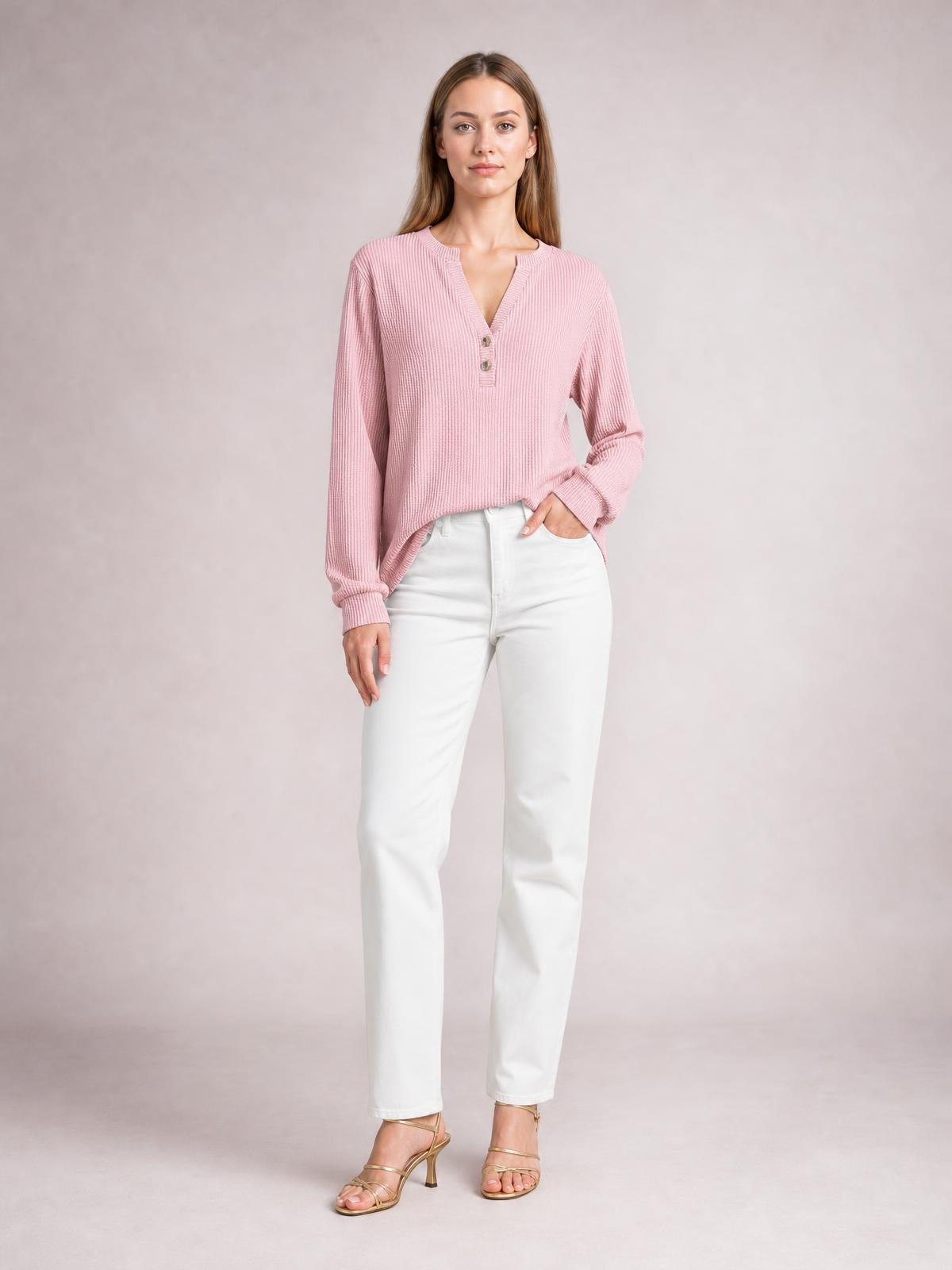 Model wears a pink striped notched long sleeve T-shirt with a relaxed silhouette, ribbed texture, and button accents, posing with one hand in her pocket.