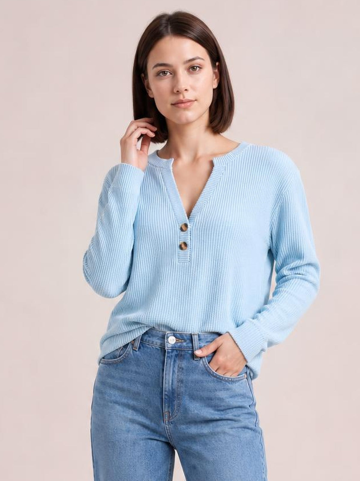 Model wearing a light blue striped notched long sleeve T-shirt with a relaxed silhouette and two button accents, posing with one hand in her jeans pocket.