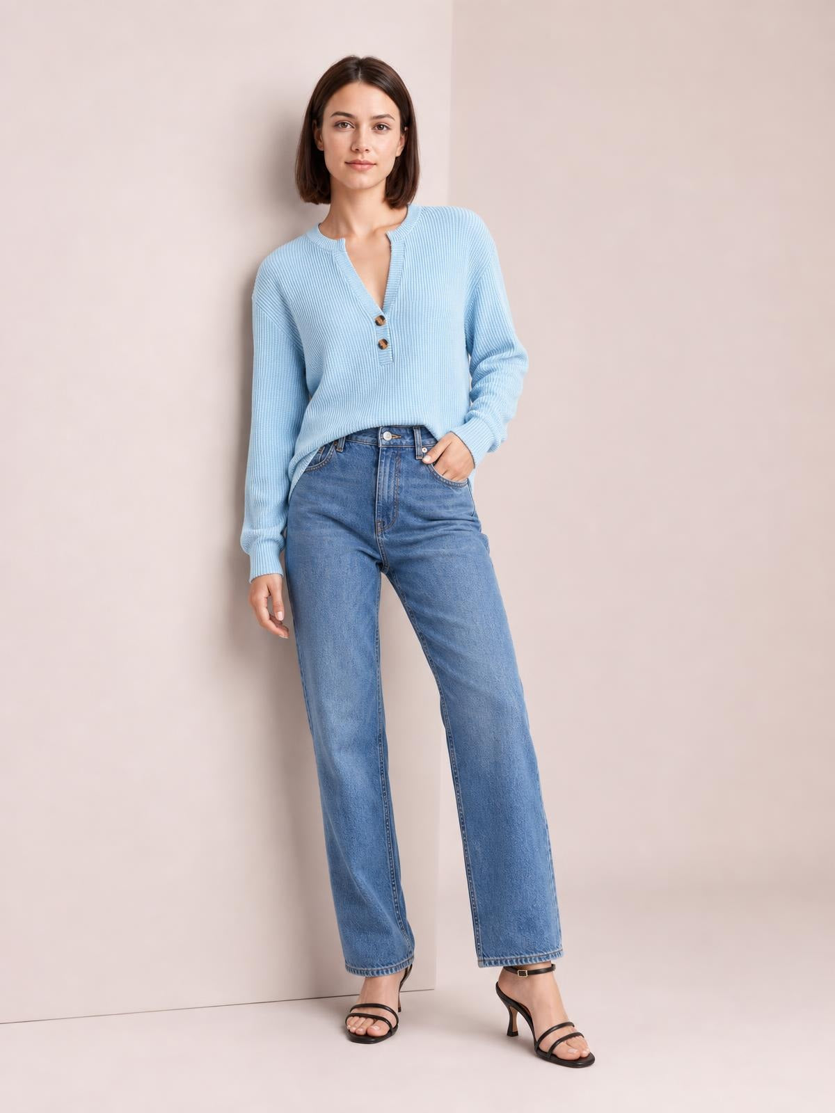 Model poses in a light blue striped notched long sleeve T-shirt with button accents and a relaxed silhouette, one hand tucked into her jeans pocket.
