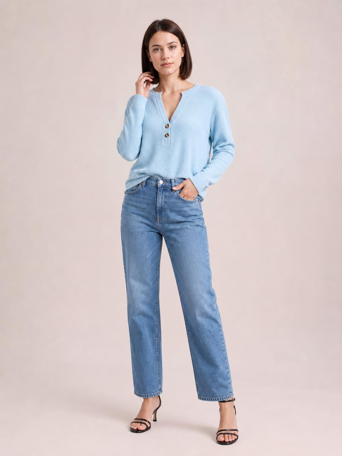 Model wears a light blue striped long sleeve T-shirt with a notched neckline, two button accents, and a relaxed silhouette, posing with one hand in her jeans pocket.
