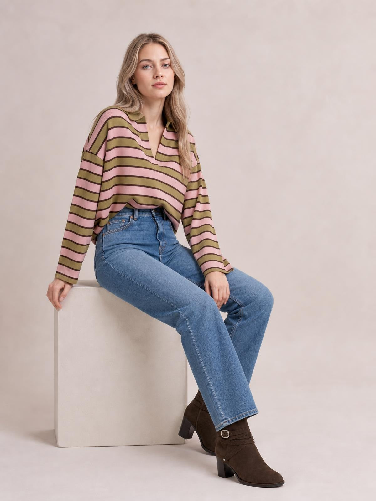 A model sits in a relaxed pose wearing a pink and olive striped long sleeve T-shirt with a notched neckline and loose, comfortable silhouette.
