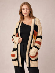 Model wears a cream striped open-front longline cardigan with black and rust accents, ribbed trim, long sleeves, and patch pockets.