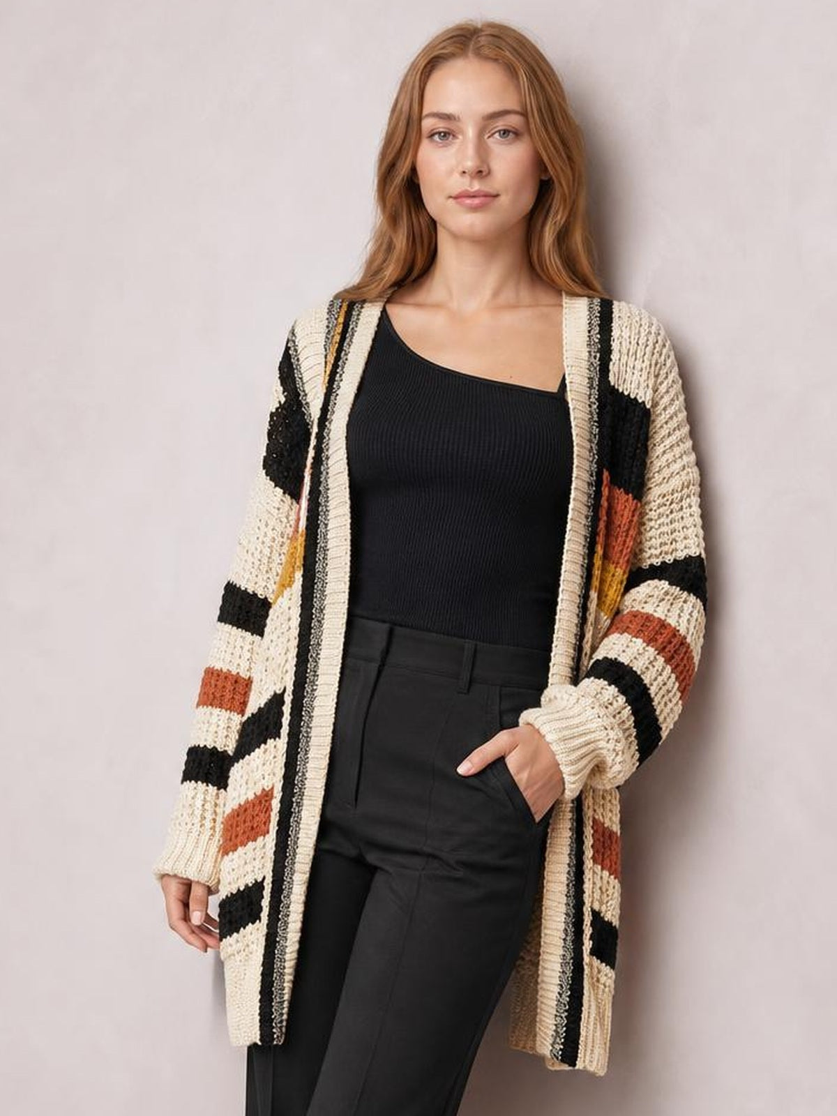 Model poses in a longline open-front cardigan with cream, black, and rust horizontal stripes, textured knit construction, ribbed cuffs, and a relaxed silhouette.
