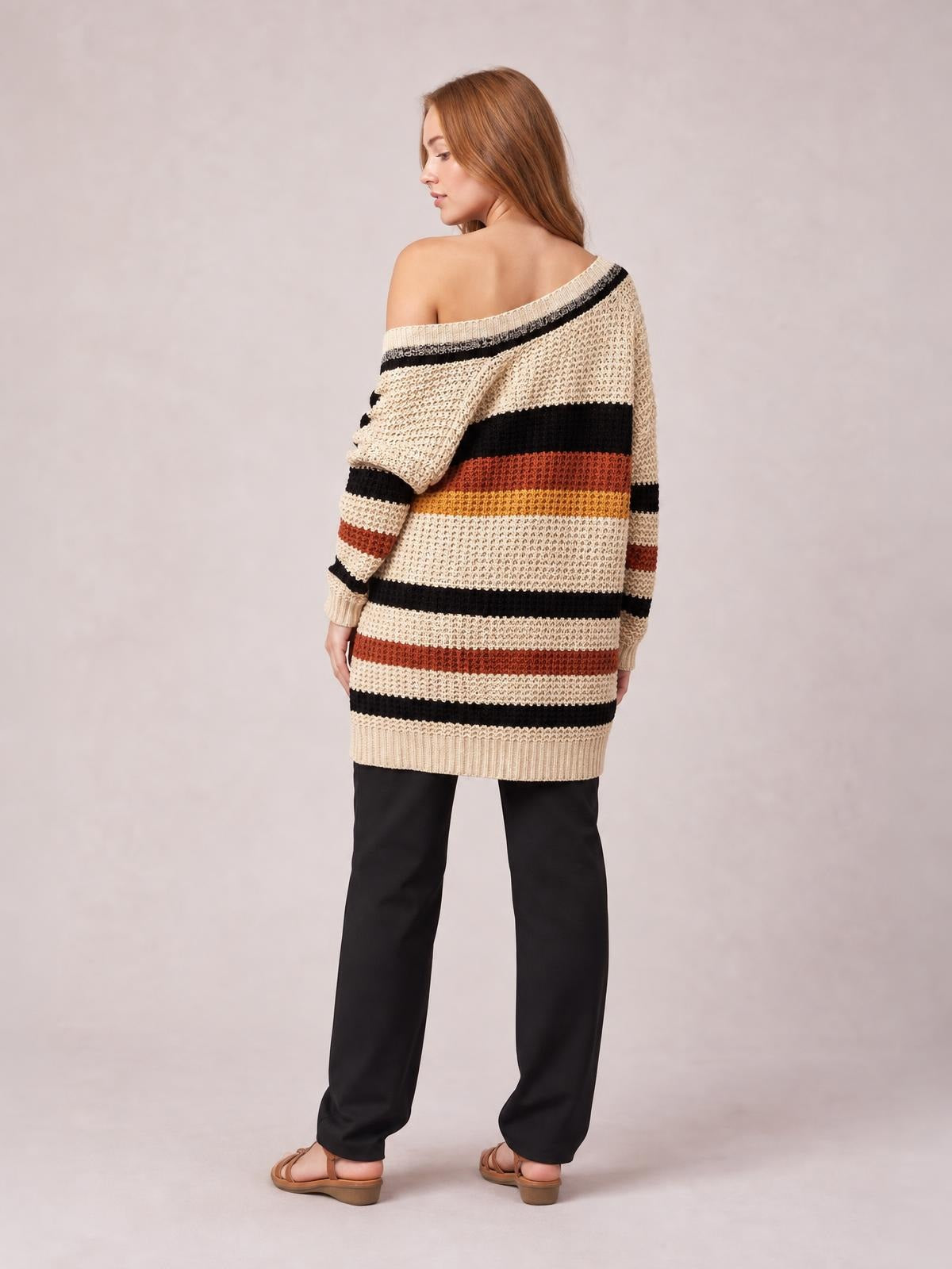 Model turns to show the back of a cream longline cardigan with black, rust, and mustard stripes, dropped shoulder, ribbed cuffs and hem, and an oversized silhouette.
