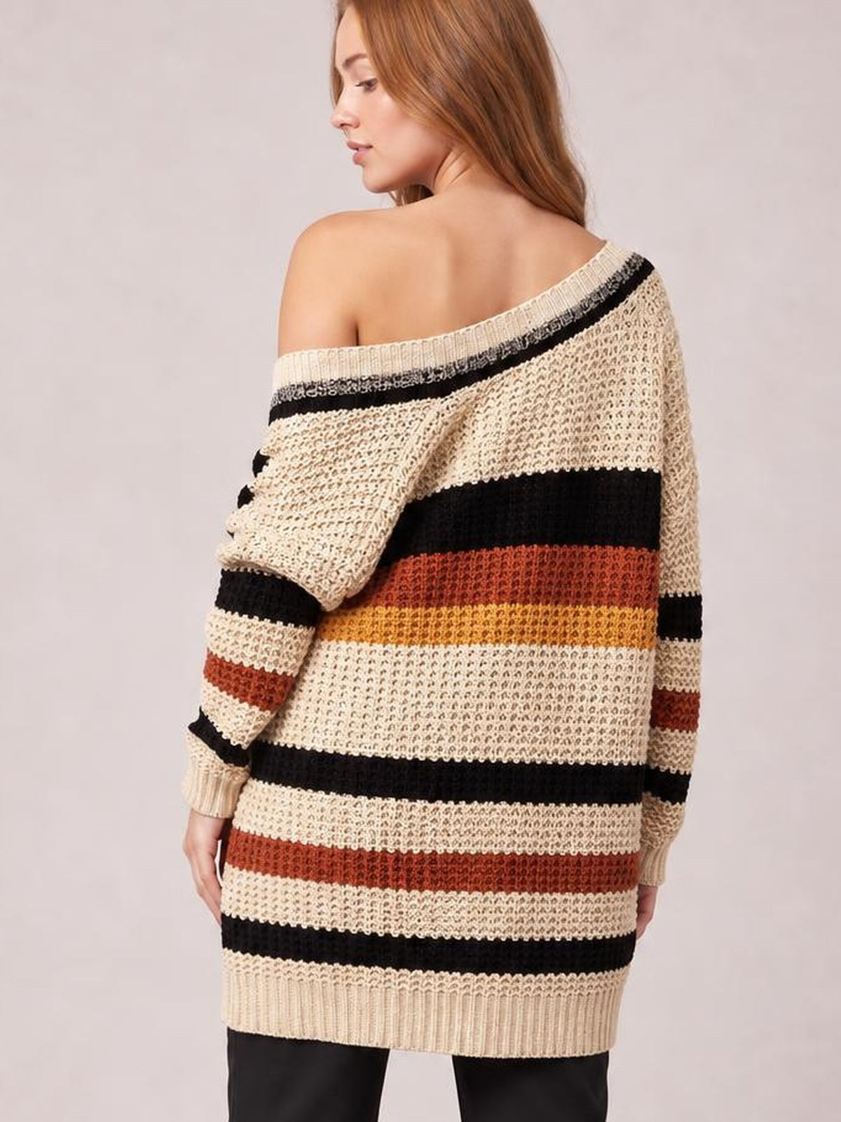 Model turned away in a relaxed longline cardigan with horizontal cream, black, rust, and mustard stripes, dropped shoulders, long sleeves, and ribbed hem and cuffs.