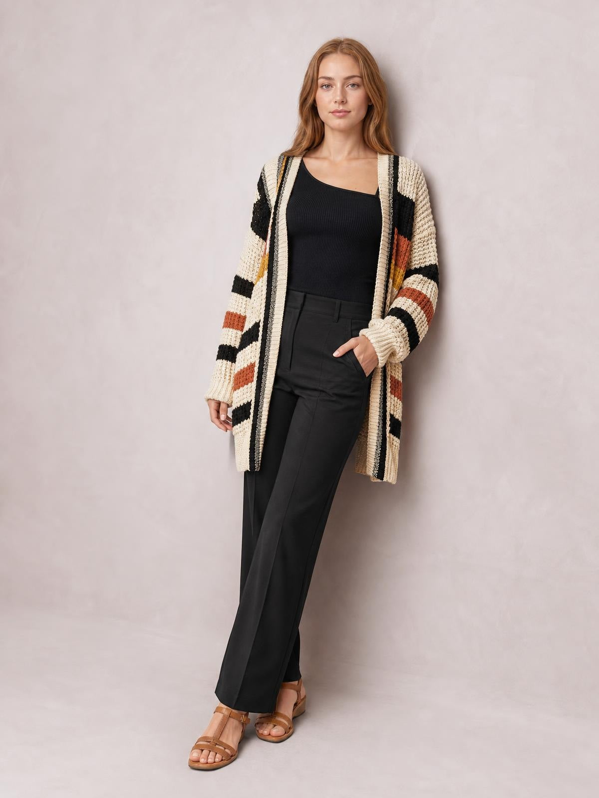 Model poses in a longline open-front cardigan with cream, black, rust, and mustard stripes, long sleeves, and a relaxed knit silhouette.