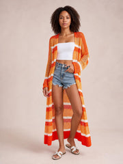 Model stands with one hand in her shorts pocket wearing a sheer orange striped open-front duster cover up with long sleeves and side slits.