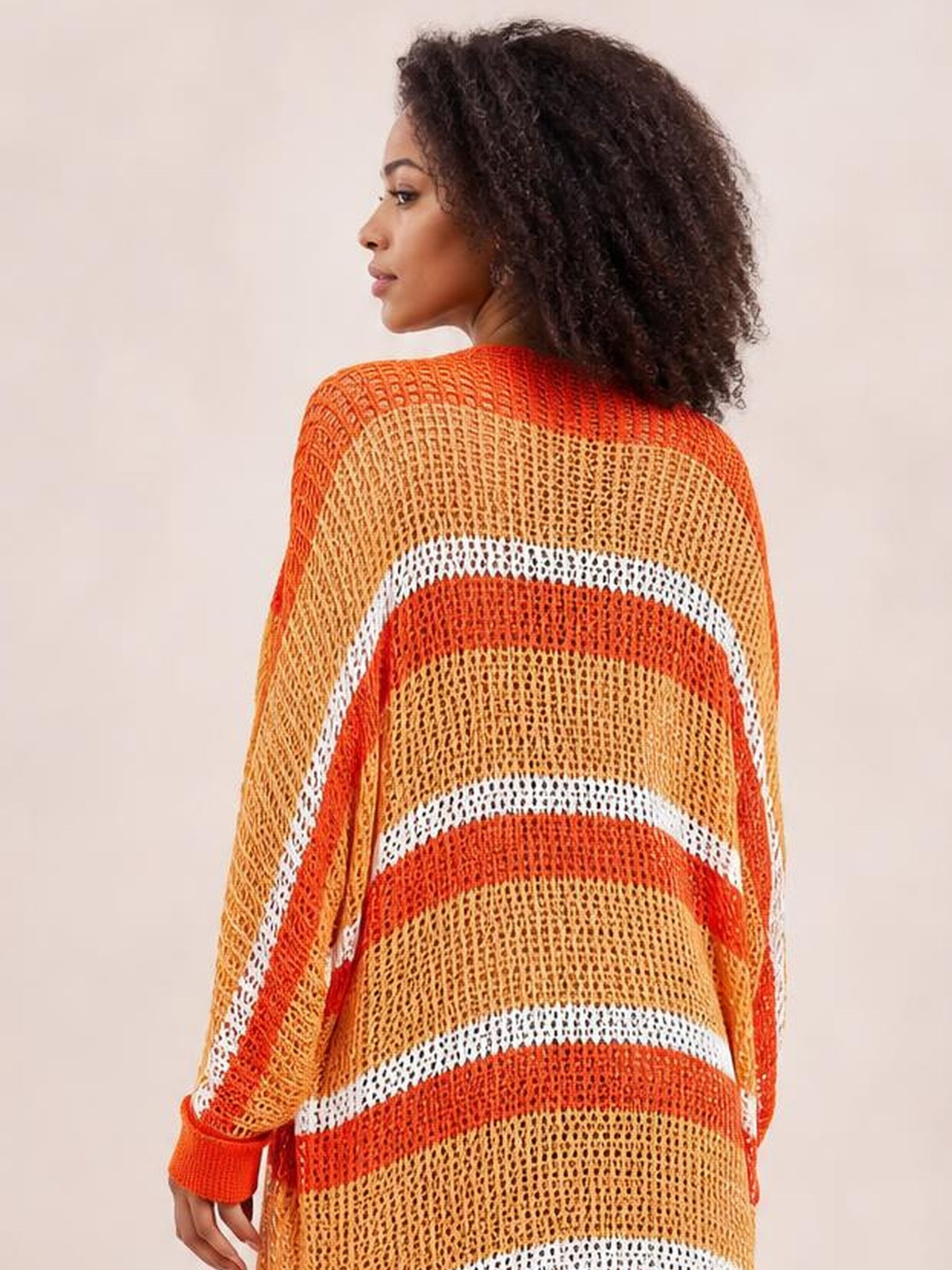 A model looks over her shoulder in a sheer striped duster cover up with orange, tan, and white bands, long sleeves, and a relaxed open-weave silhouette.