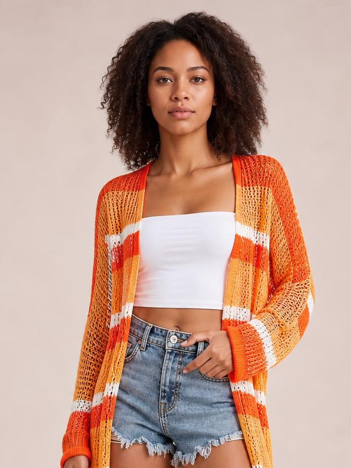 Model wears an orange, white, and yellow striped sheer open-front duster cover-up with long sleeves and a relaxed longline silhouette over a white crop top.