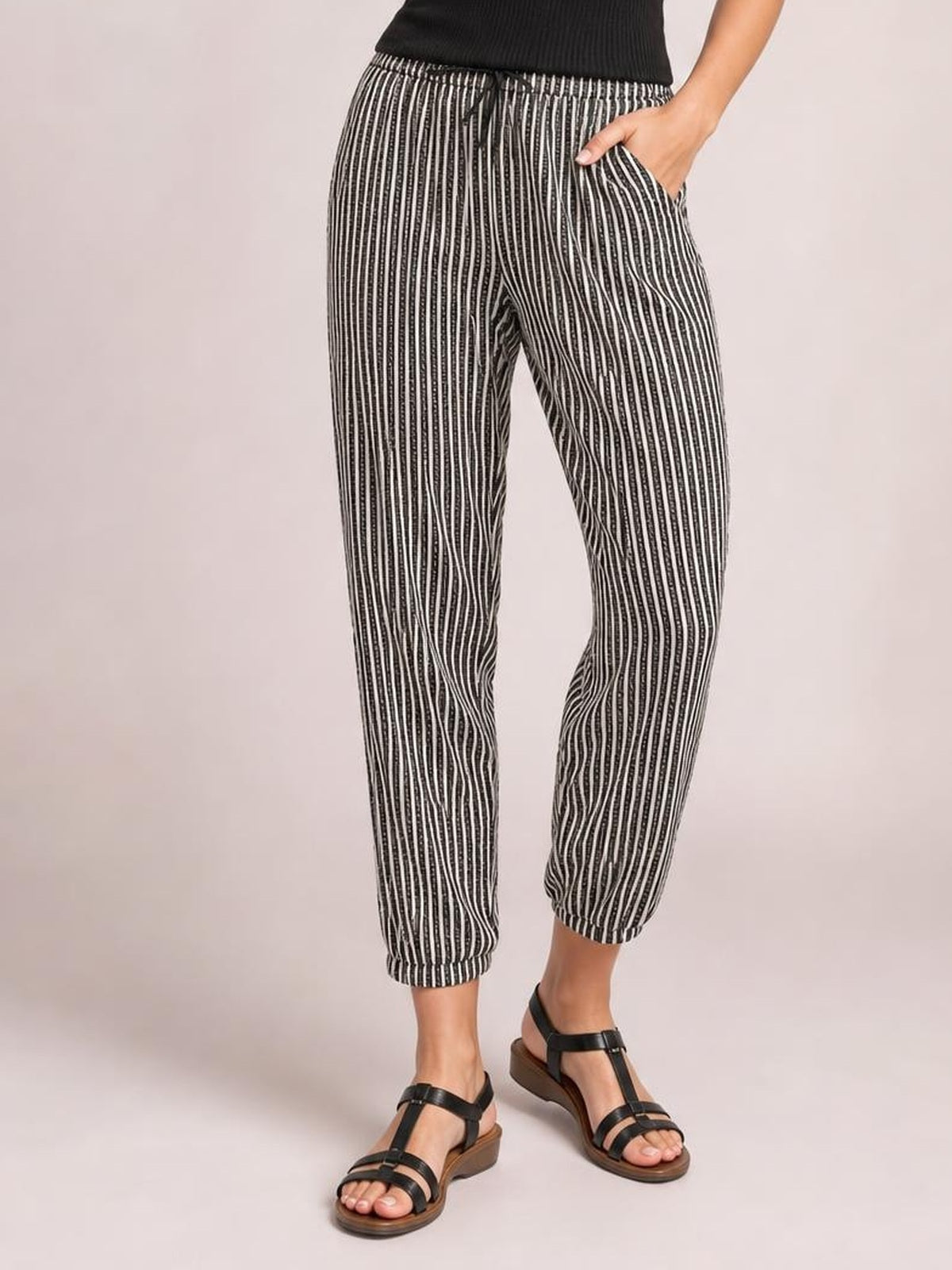 Model wearing black-and-white striped pants with an elastic drawstring waist, side pockets, relaxed tapered silhouette, and cropped elastic cuffs.