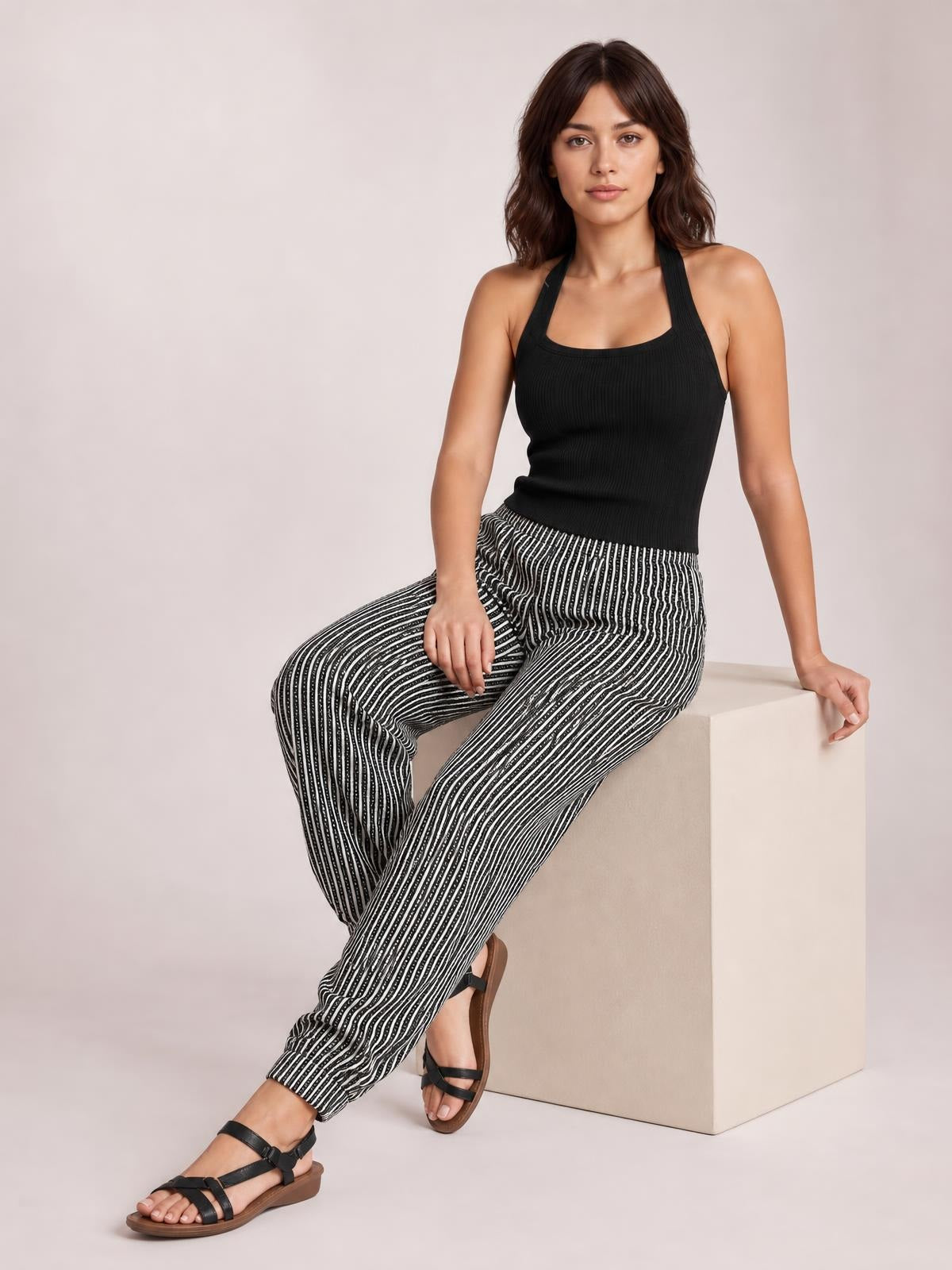 Model seated in black and white striped pants with pockets, featuring a relaxed straight-leg silhouette and elasticized waist.