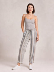A woman models striped pants with gray and white vertical stripes, a relaxed straight-leg silhouette, drawstring waist, side pockets, and cuffed hems.