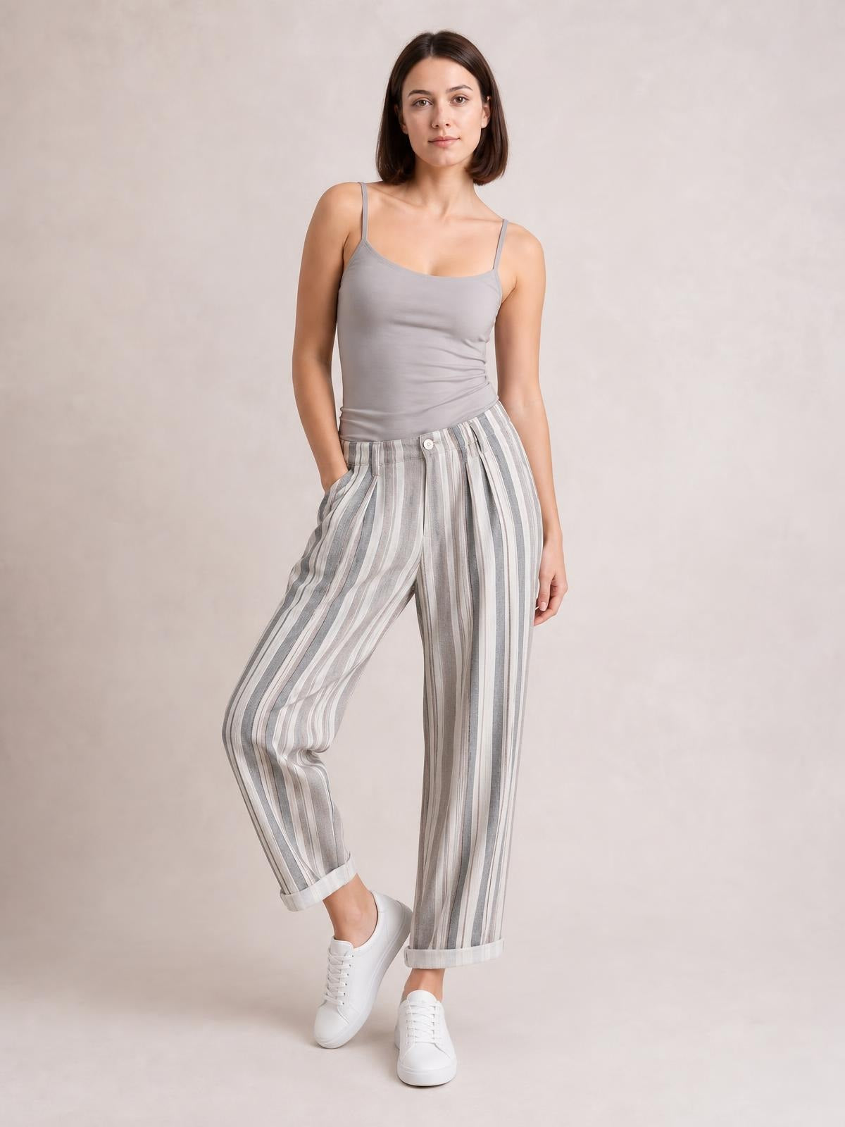 Model wearing gray and white striped pants with pockets, a relaxed tapered silhouette, button closure, and rolled cuffs while posing with one leg bent.