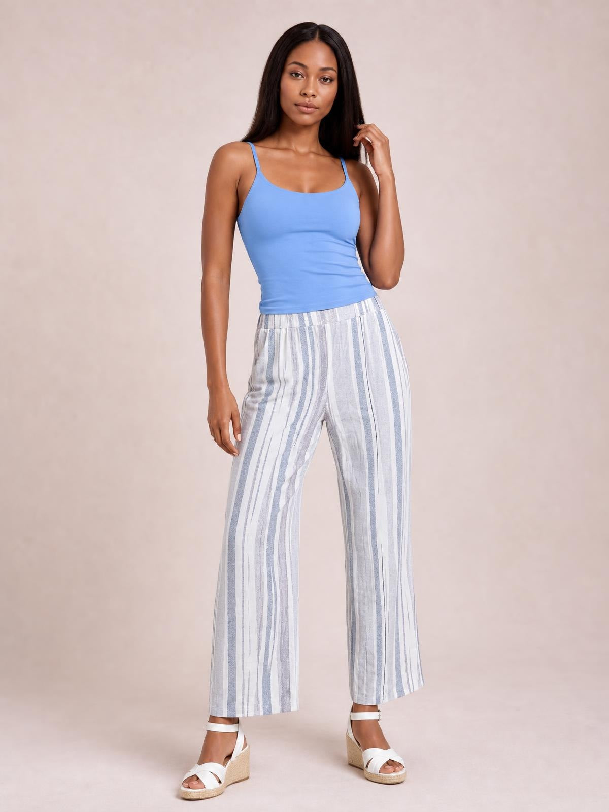 A model poses in white and light blue striped pants with a relaxed wide-leg silhouette, cropped hems, gathered waistband, and practical pockets.