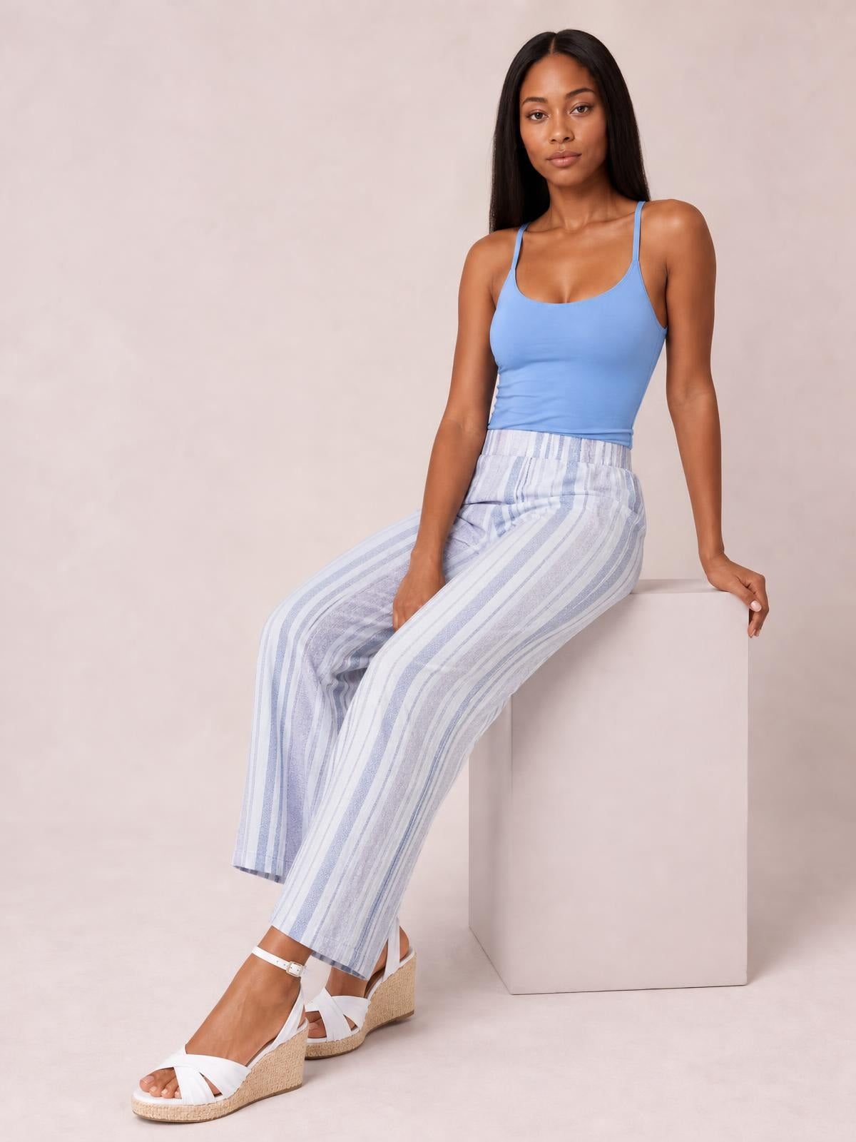 A seated model wears opaque blue-and-white striped pants with a high waist, relaxed wide-leg silhouette, and practical side pockets.