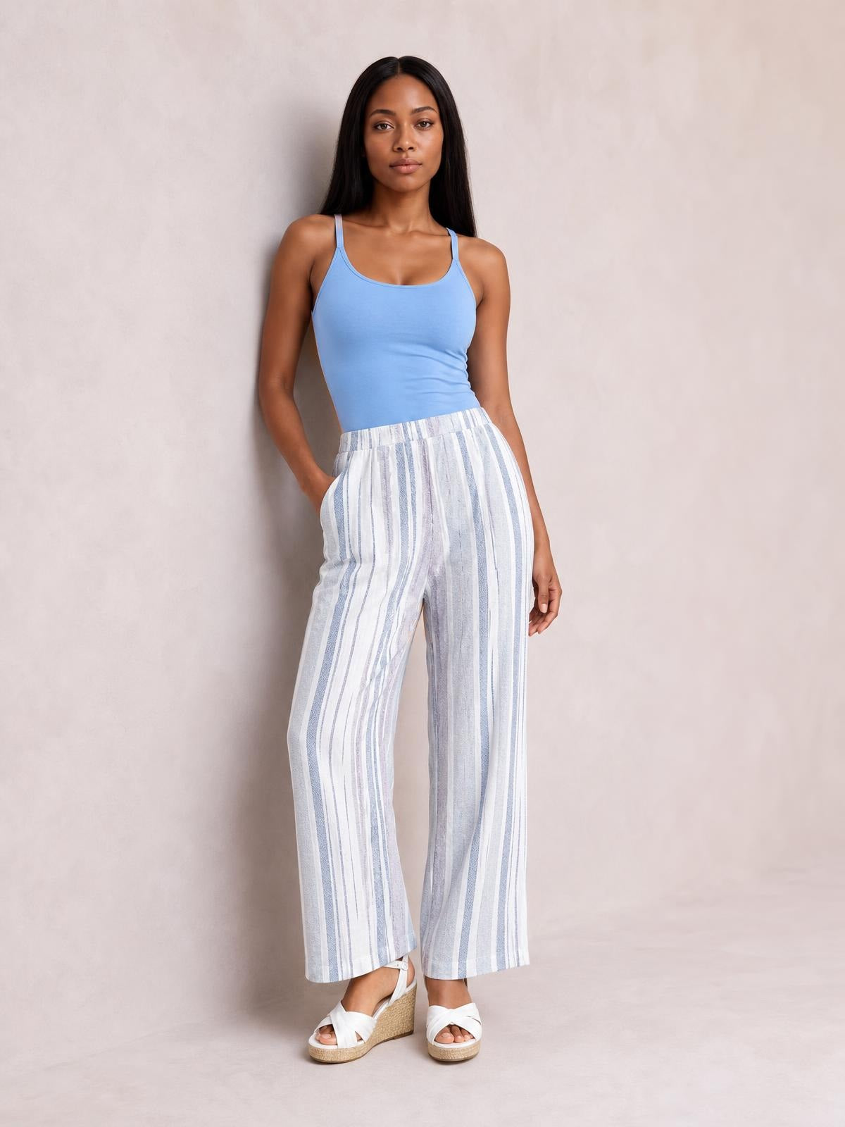 Model poses with one hand in the pocket of white and light blue striped pants, featuring a relaxed wide-leg silhouette and cropped straight hems.