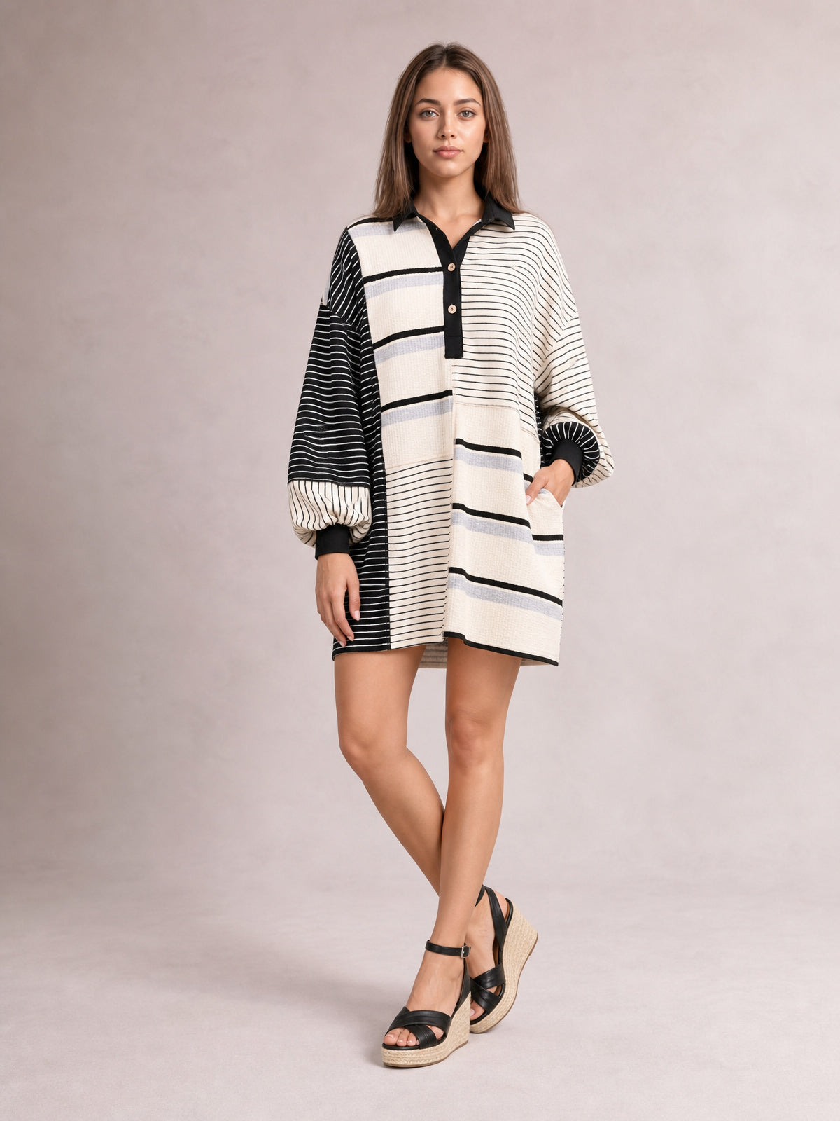 Model poses in a relaxed stance wearing a black-and-ivory striped patchwork long sleeve mini dress with a loose silhouette, button front, and collared neckline.