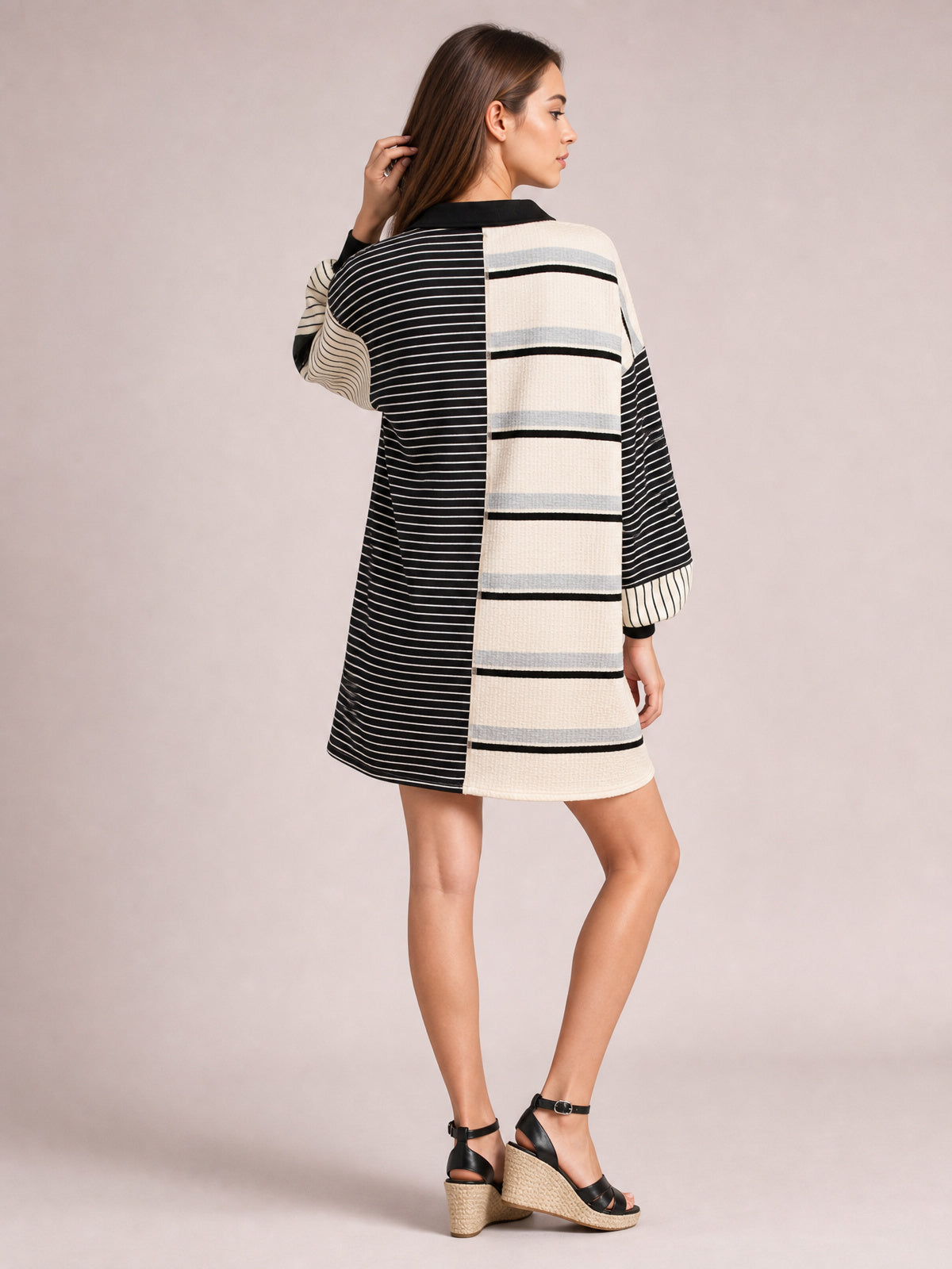 Model poses in a relaxed stance wearing a black-and-ivory striped patchwork long sleeve mini dress with contrasting panels and an easy silhouette.