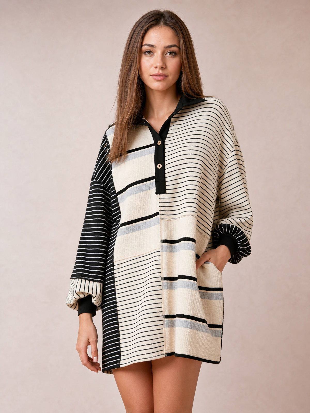 Model poses in a relaxed stance wearing a black-and-ivory striped patchwork long sleeve mini dress with a loose silhouette, button front, and contrasting stripe directions.
