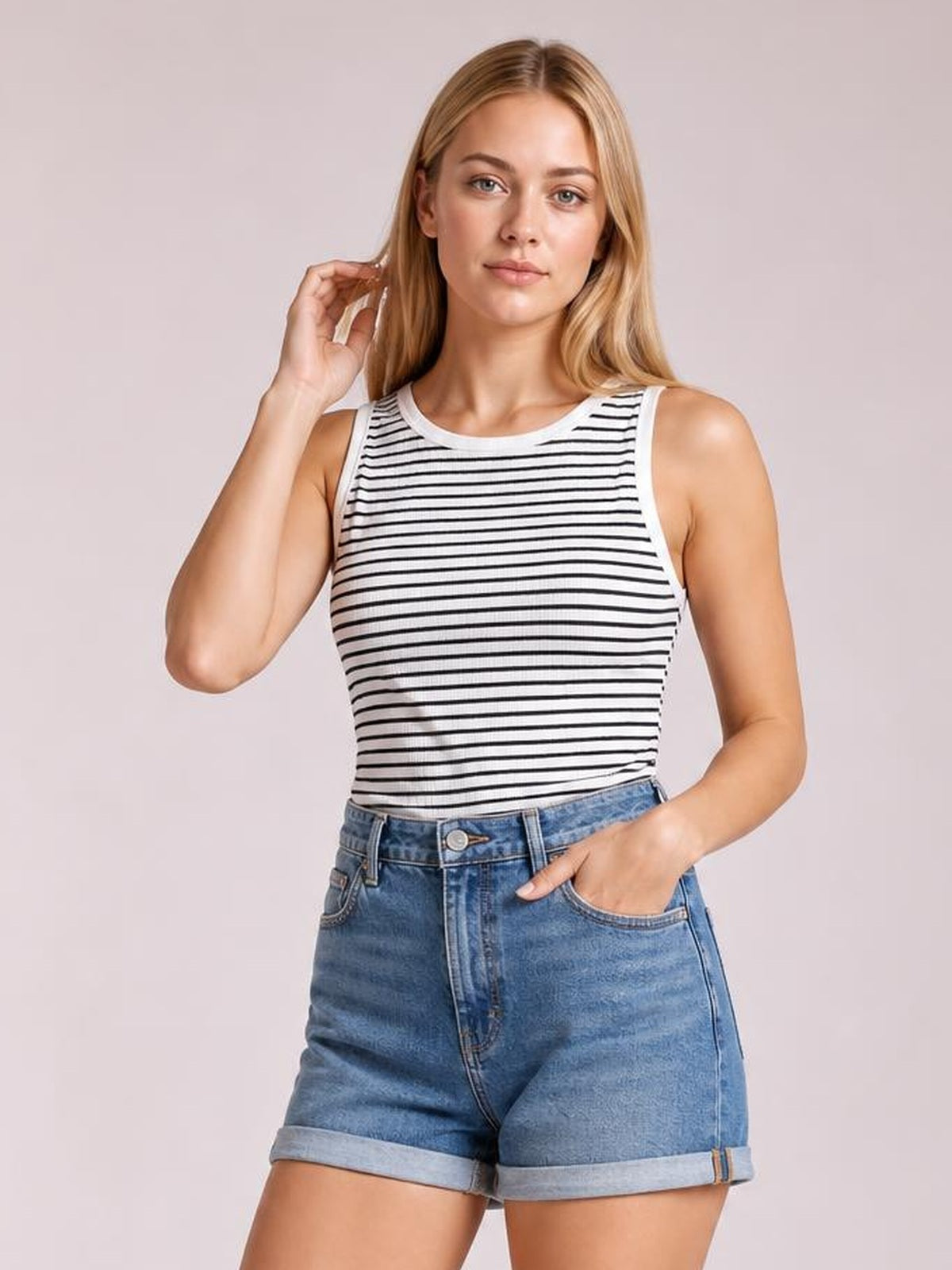 Model poses with one hand in her pocket and one touching her hair, wearing an opaque striped ribbed tank with a round neck and fitted silhouette.